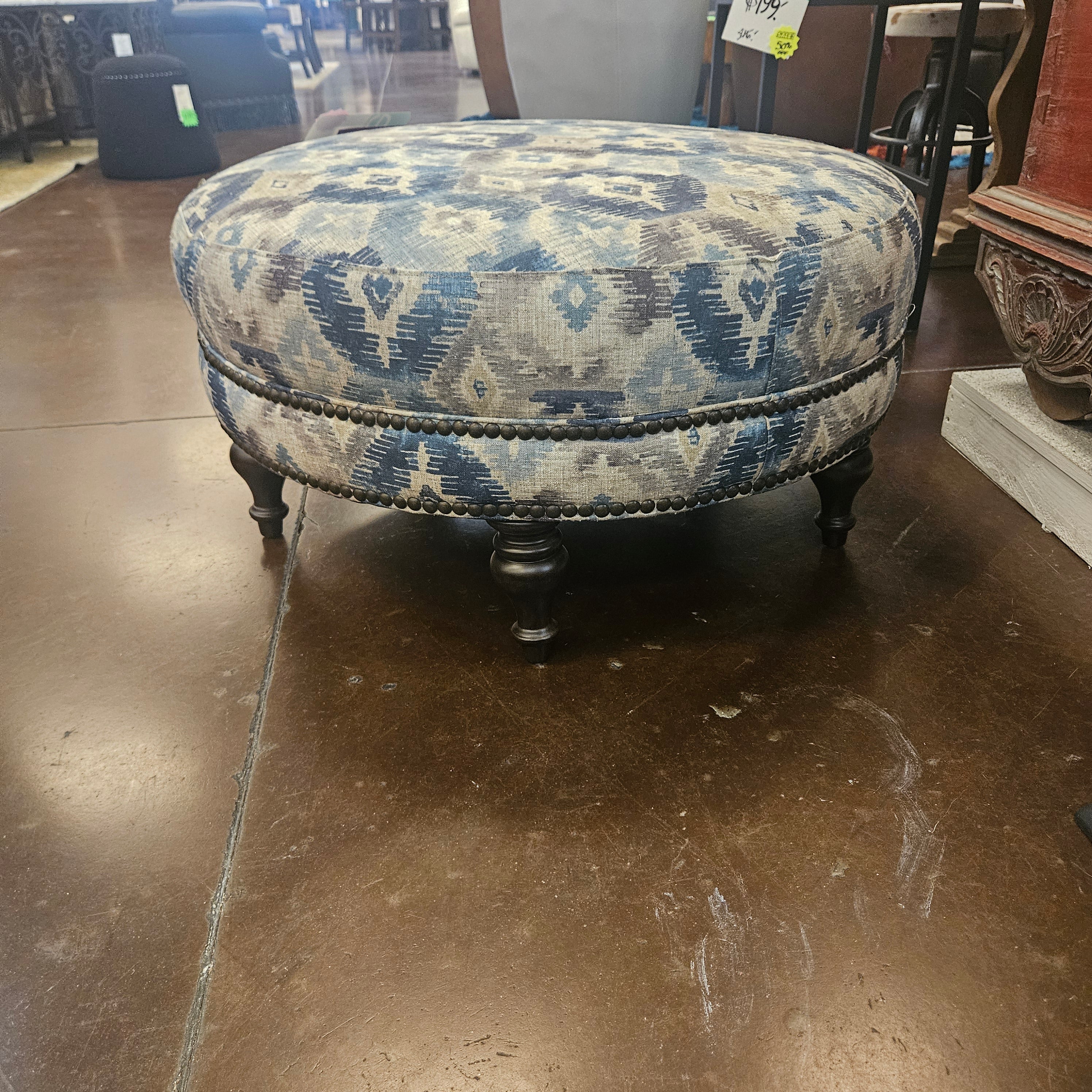 Round patterned ottoman on a brown floor with a blurred background