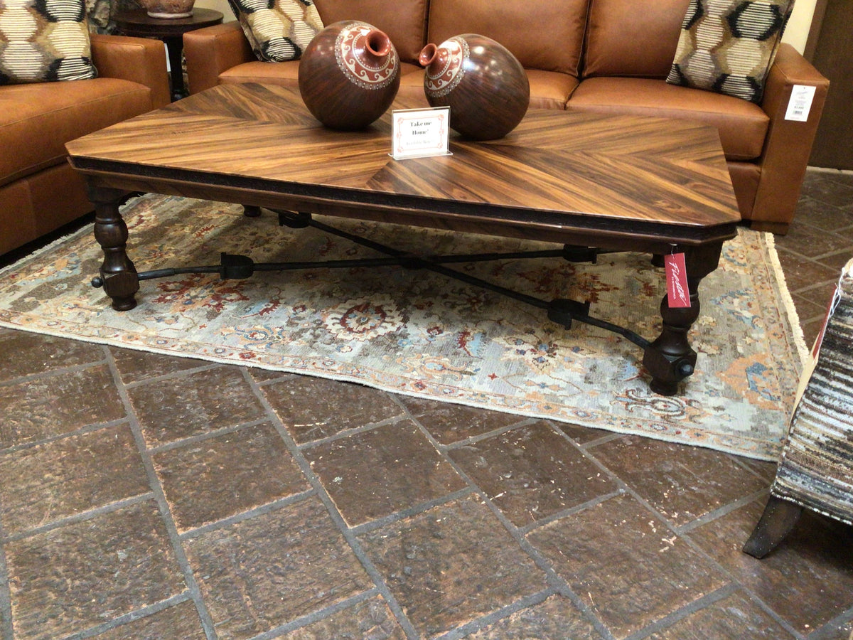 Wooden coffee table with decorative vases on a patterned rug in a showroom setting.