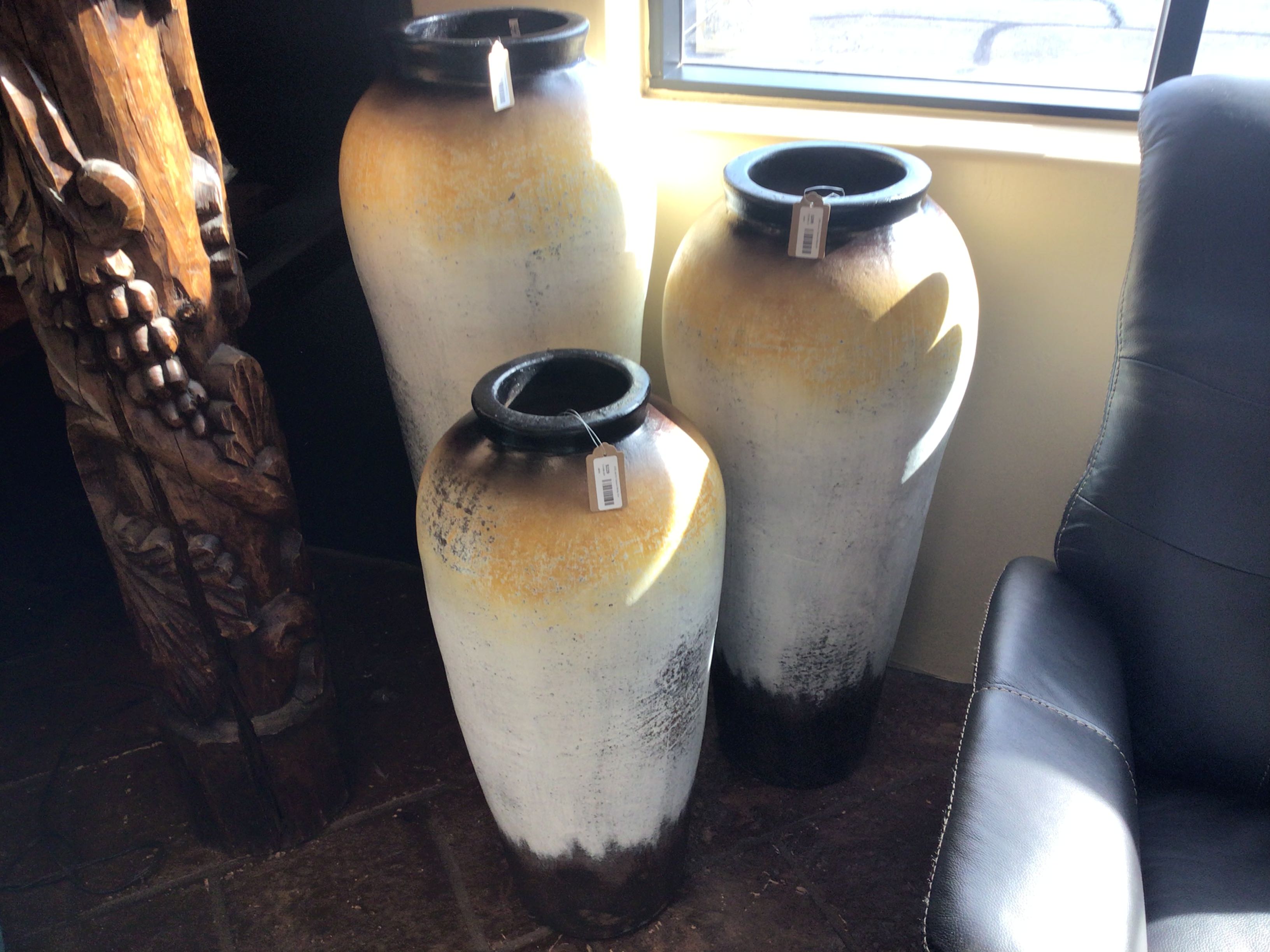 Three large ceramic vases on a tiled floor with a window in the background.