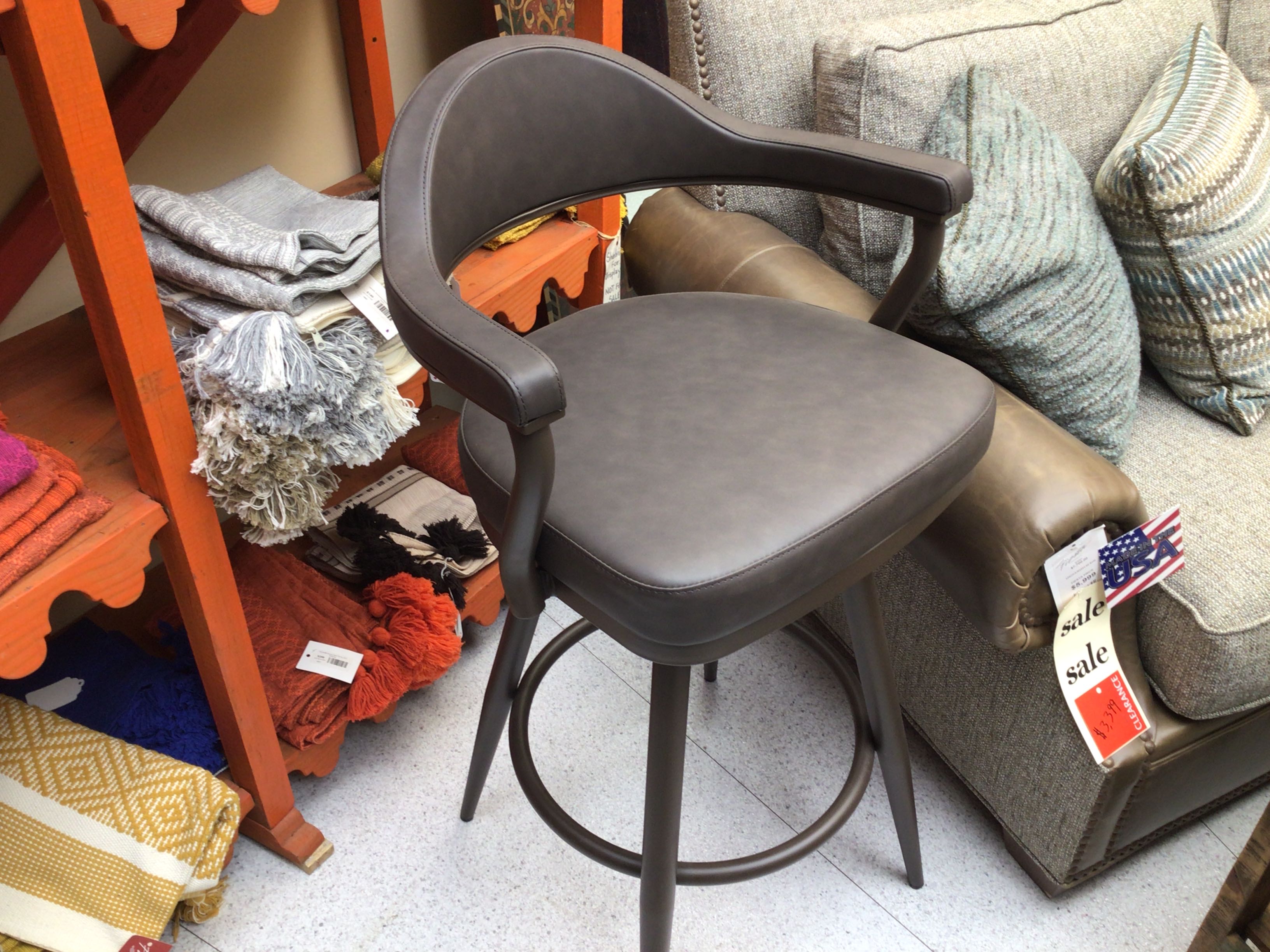 Gray bar stool in a store setting with furniture and clothing in the background