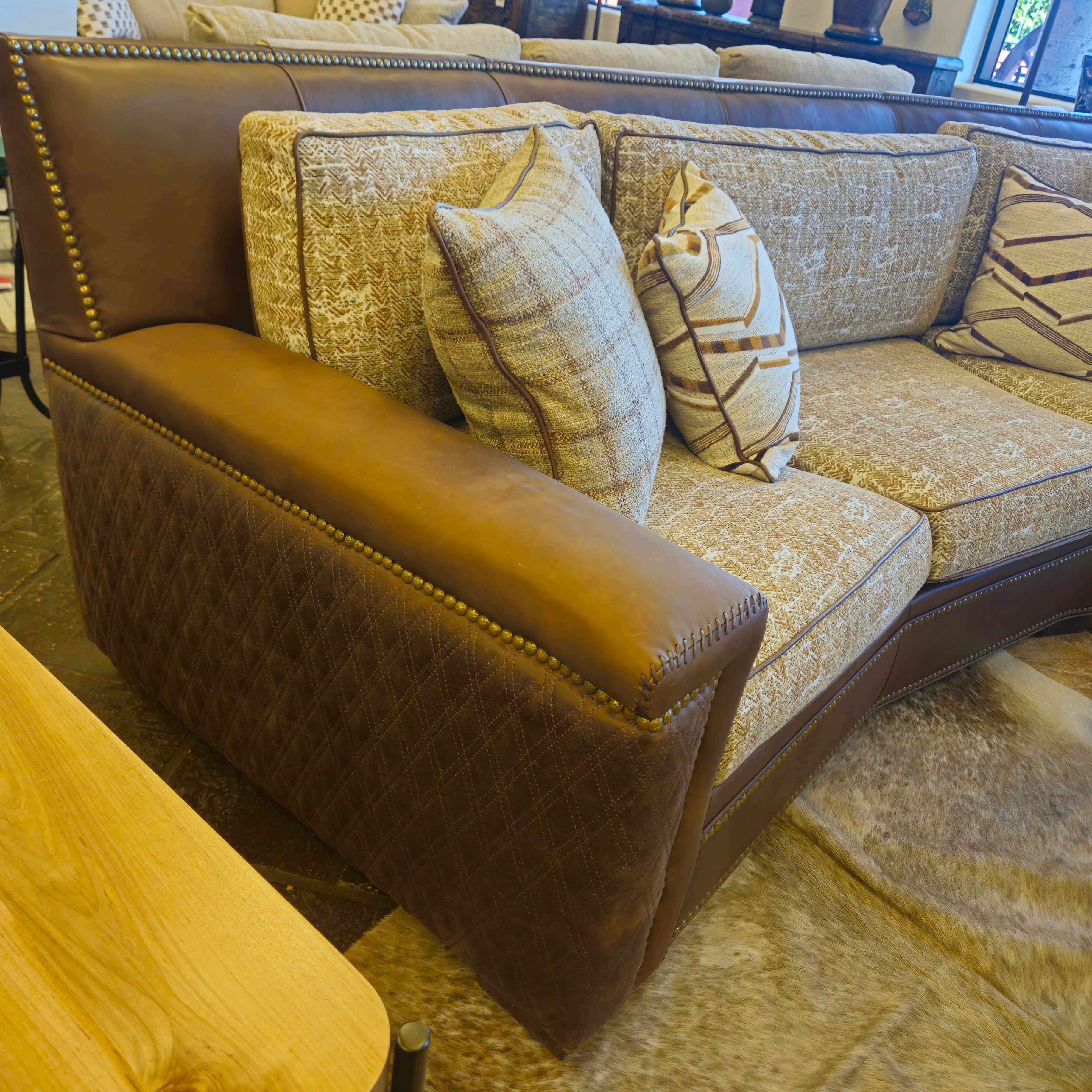 Brown leather and patterned fabric sofa with decorative pillows in a showroom setting.