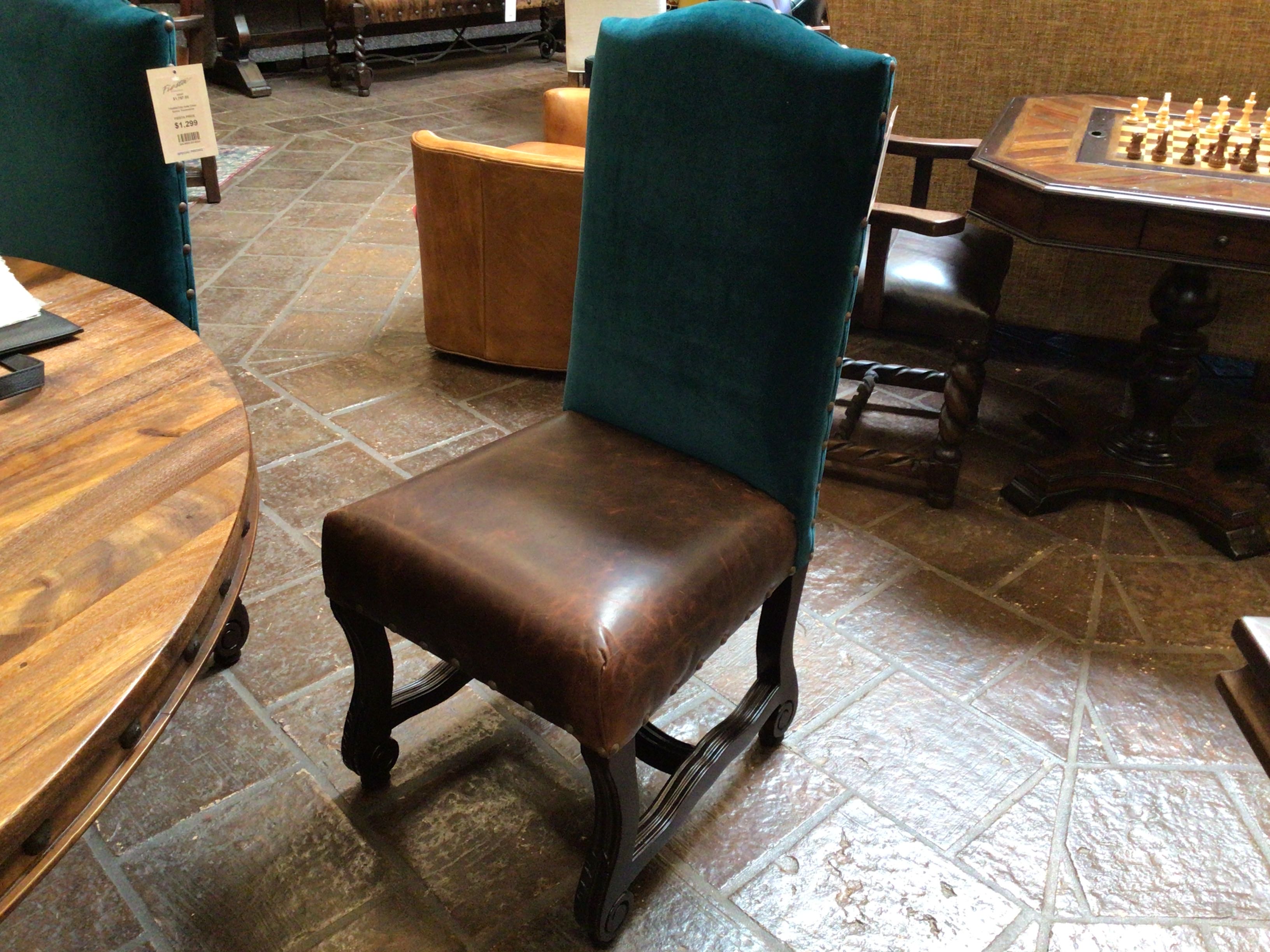 Chair with brown leather seat and teal velvet backrest in a room with tiled floor and furniture.