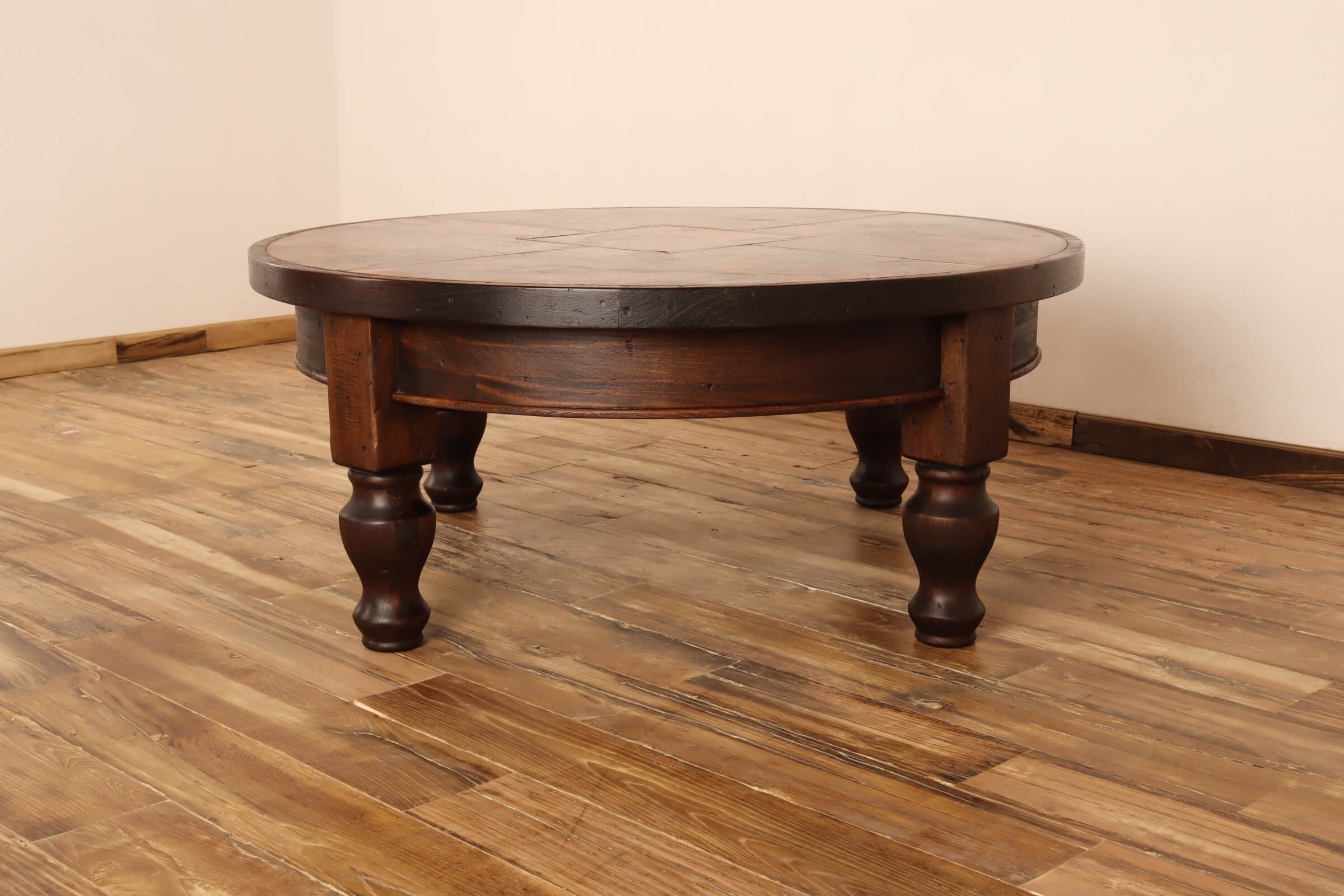 Round wooden table on a wooden floor with a plain wall background