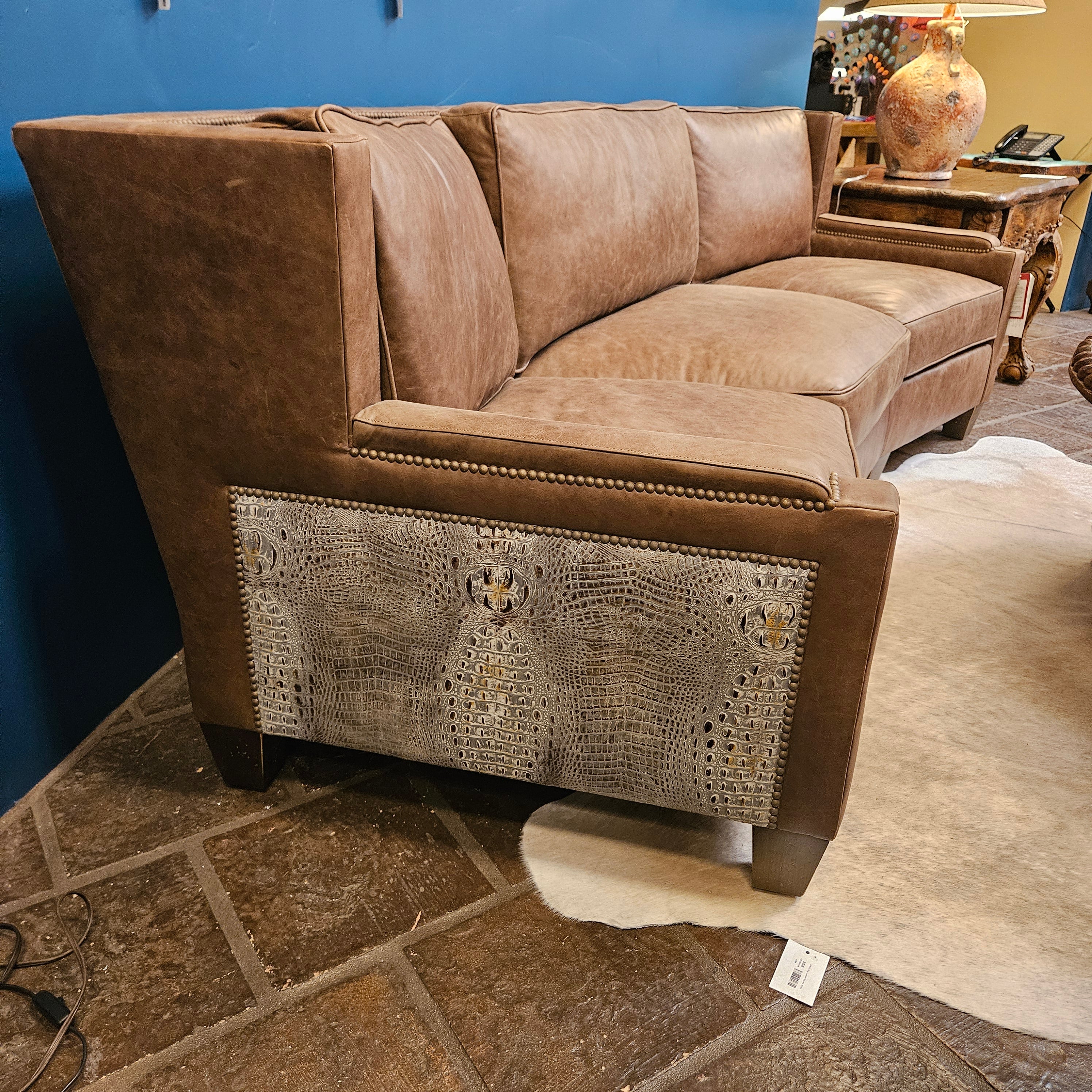 Brown leather sofa with decorative pattern on a stone floor against a blue wall.
