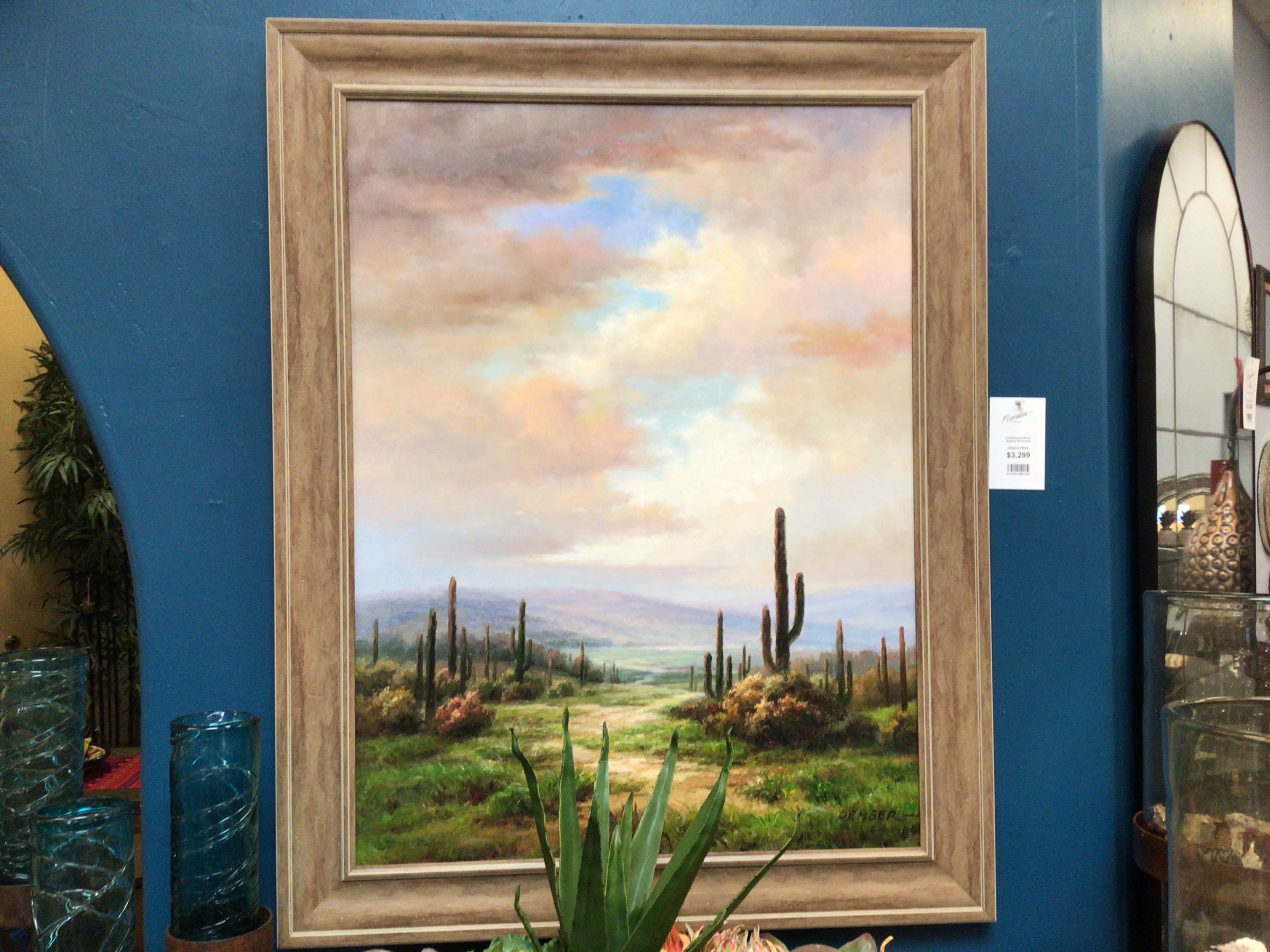 Framed painting of a desert landscape with cacti on a blue wall.