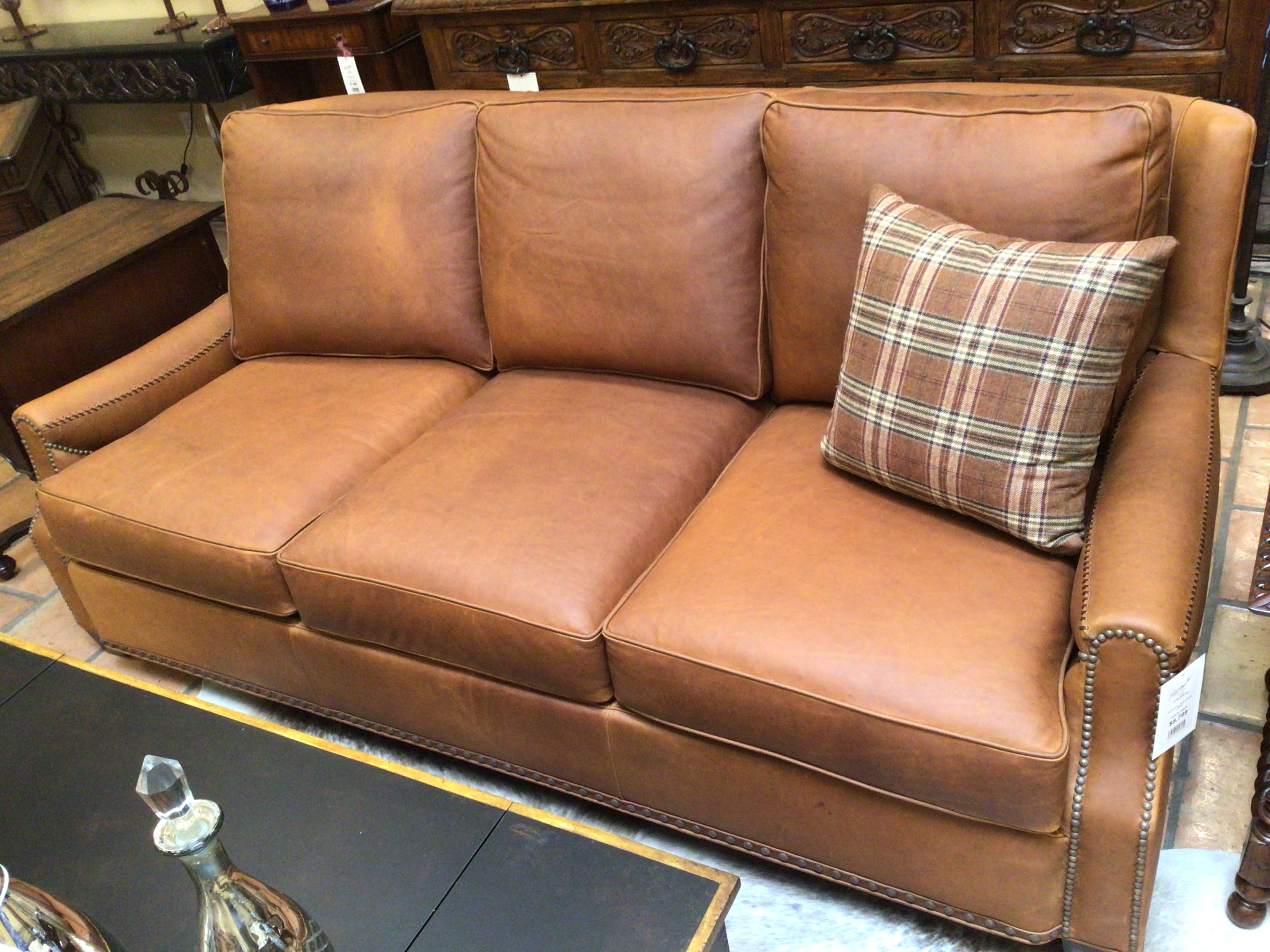 Brown leather sofa with a plaid pillow in an indoor setting