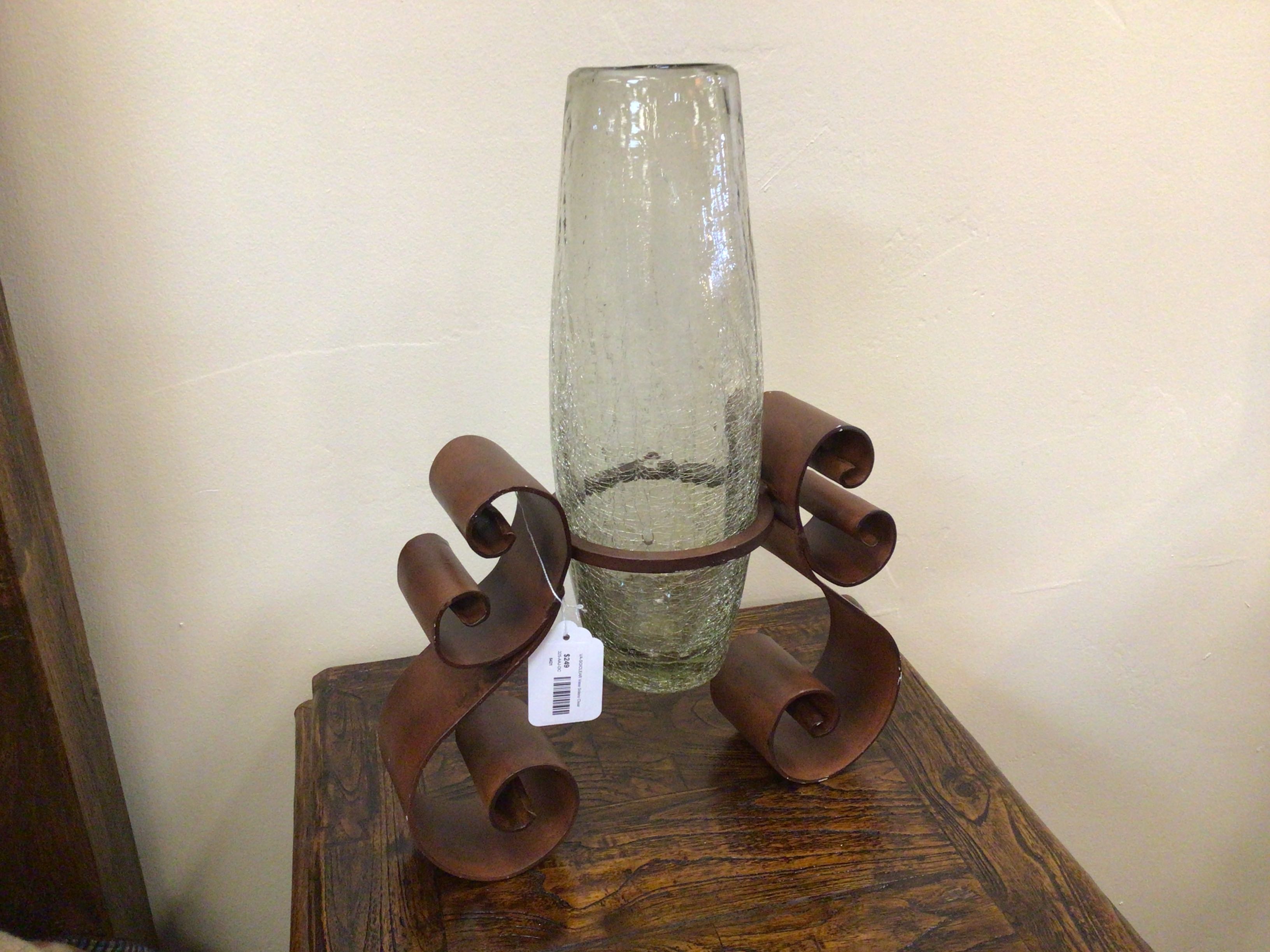 Decorative glass vase on a unique metal stand against a plain background
