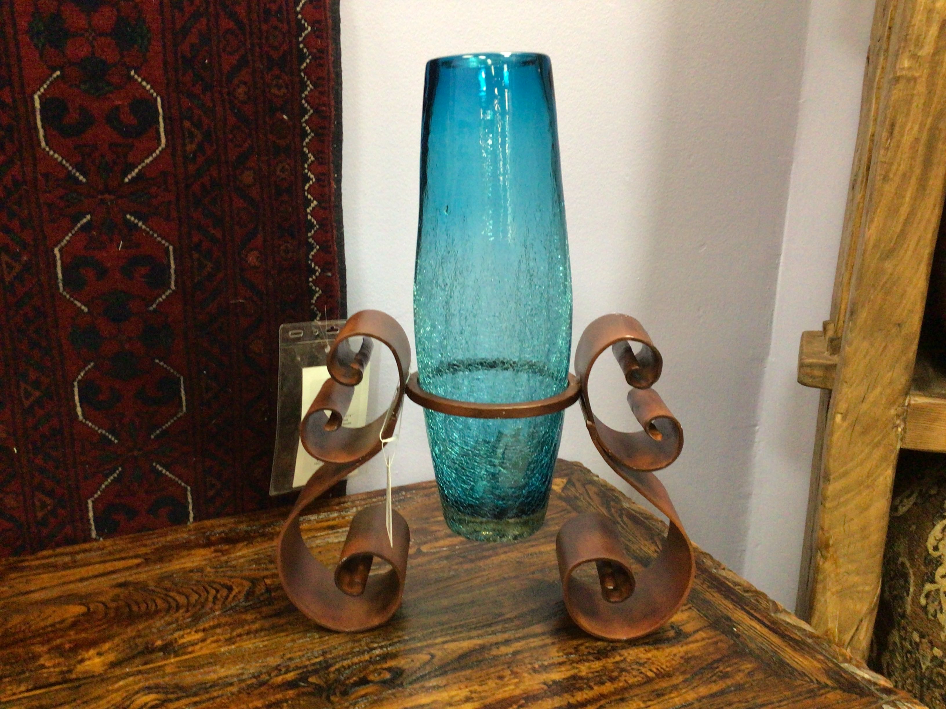 Blue glass vase on a decorative metal stand on a wooden surface.