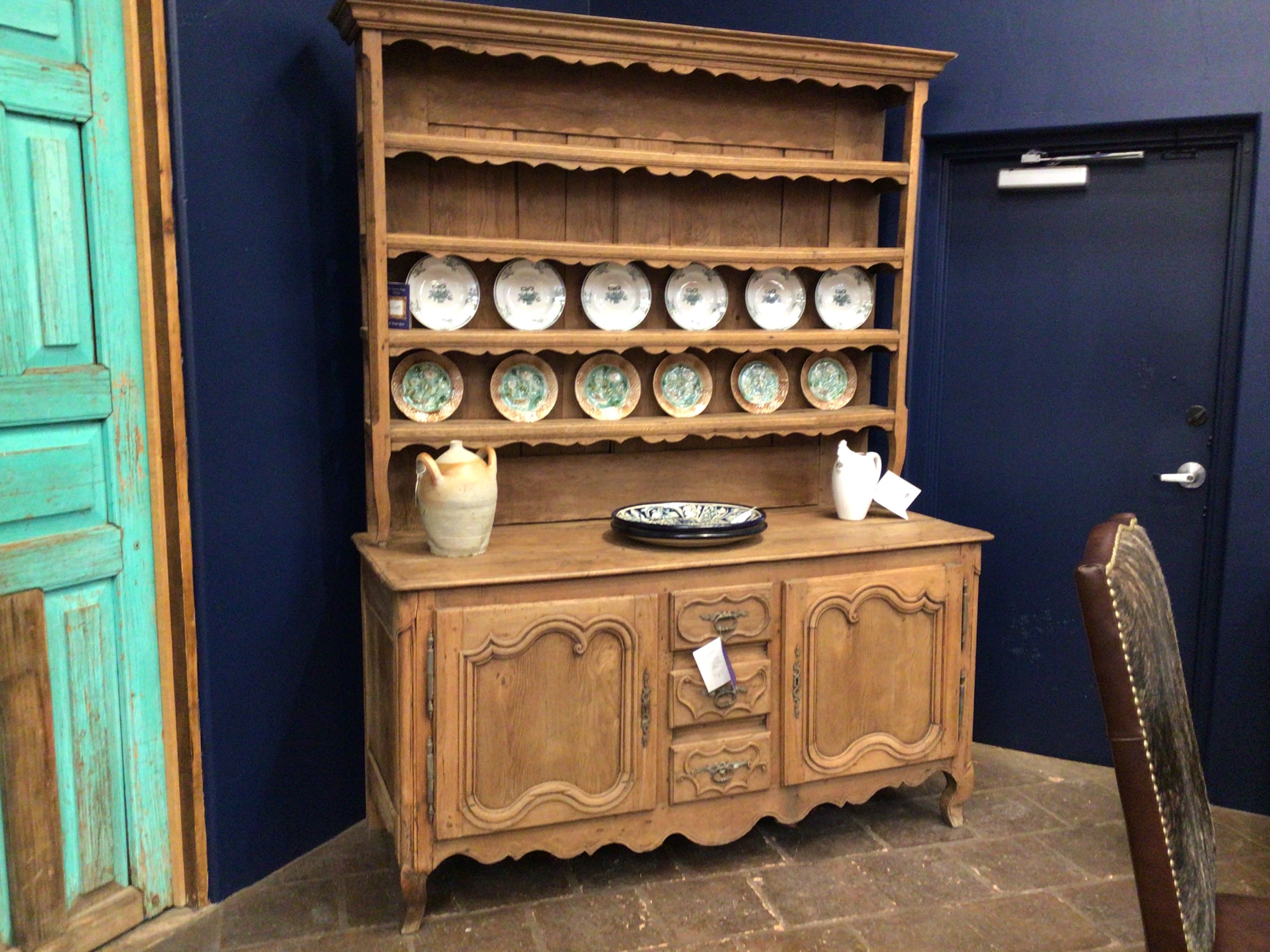 Wooden cabinet with decorative plates and a chair against a blue wall.