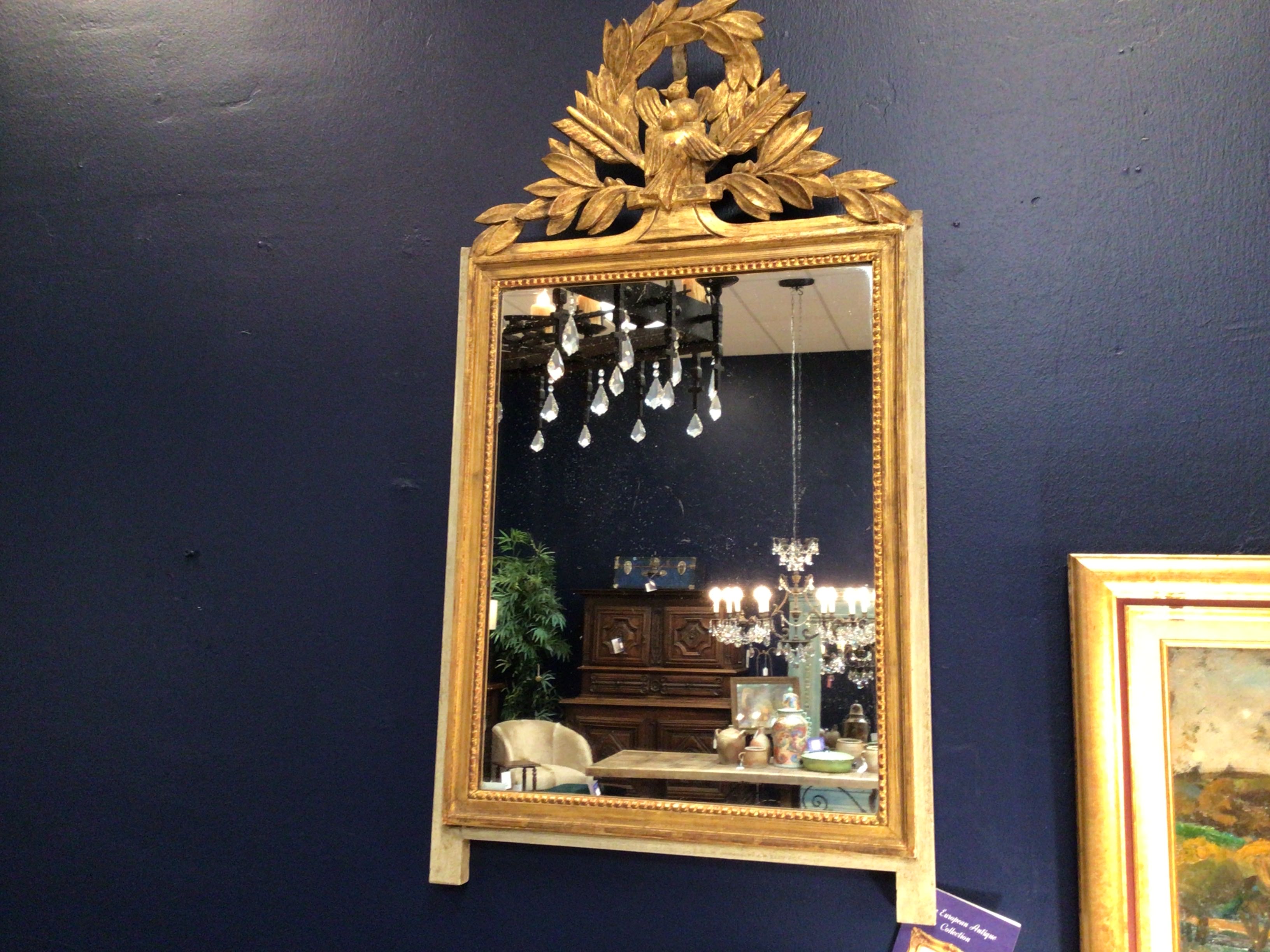 Gold-framed mirror on a dark blue wall with a chandelier reflection