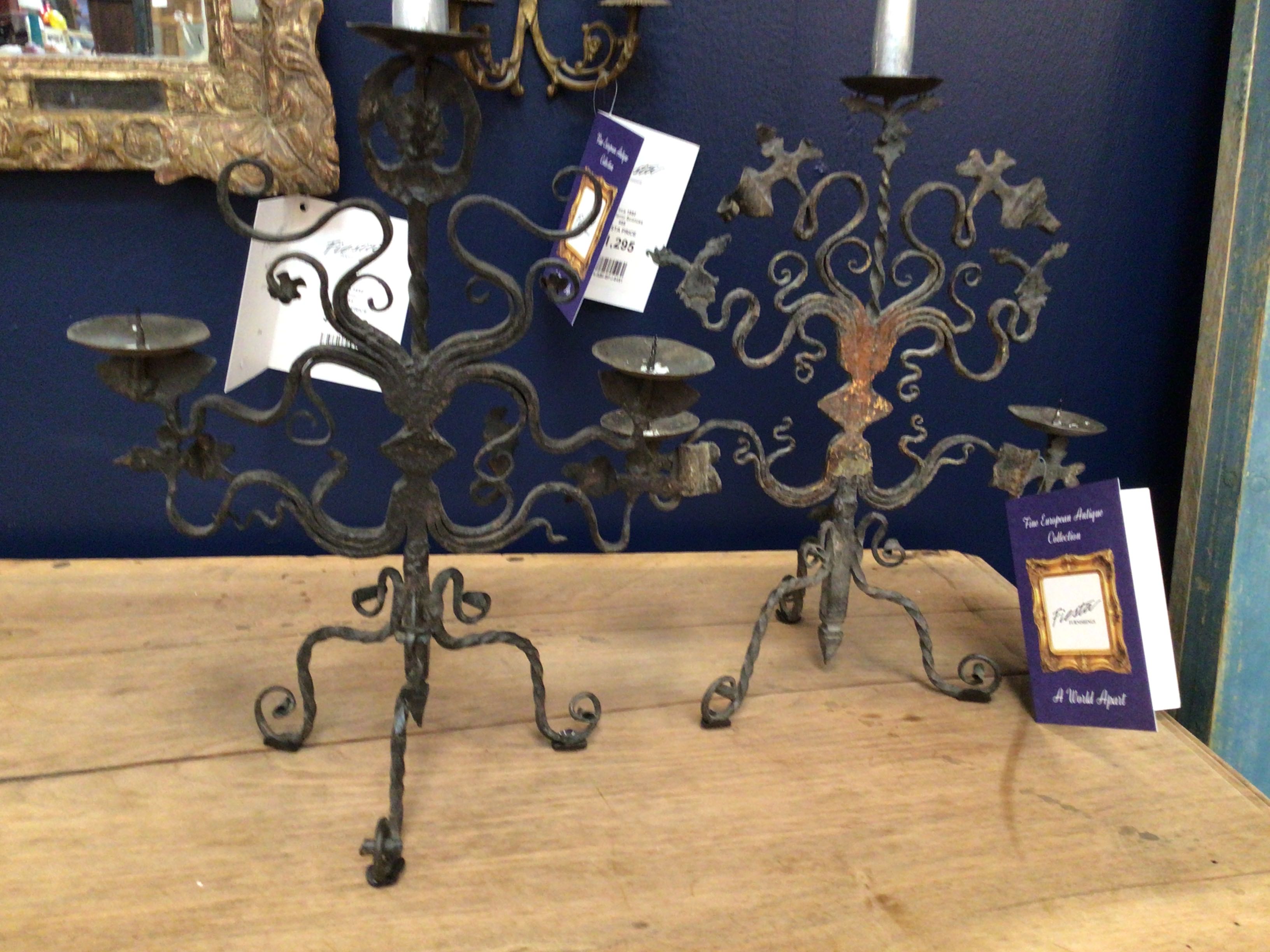 Two ornate metal candelabras on a wooden surface with a blue wall in the background.