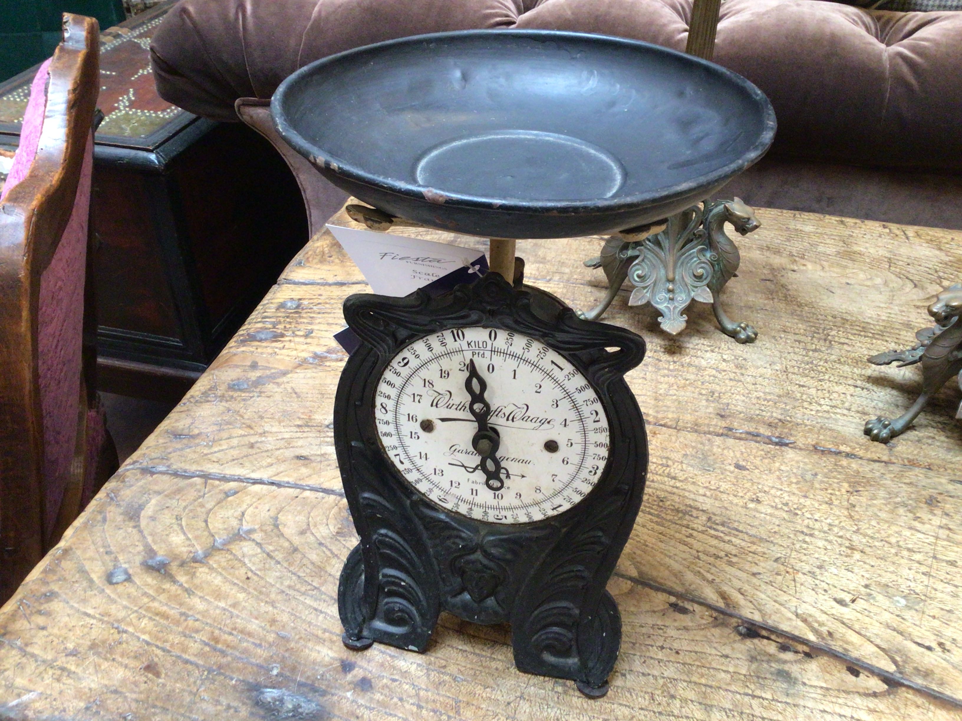 Vintage-style scale on a wooden surface with a brown cushioned chair in the background.