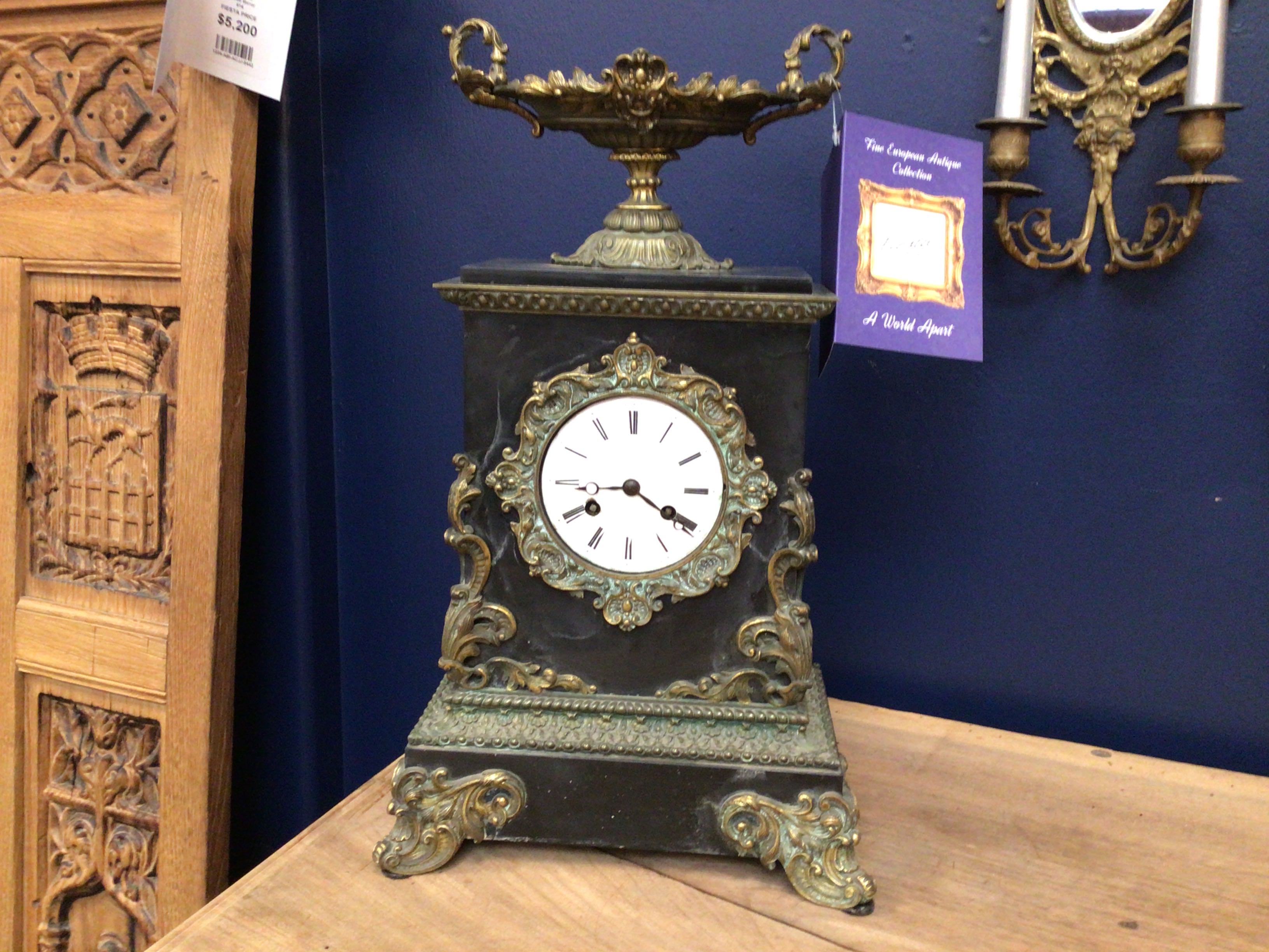 Decorative clock with ornate design on a wooden surface against a blue wall.