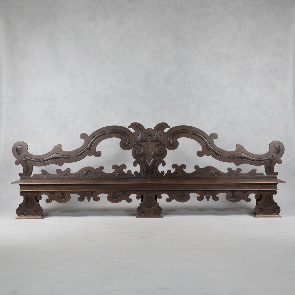 An ornate dark brown carved wooden bench with elaborate scrollwork and decorative legs, photographed against a neutral gray studio backdrop.