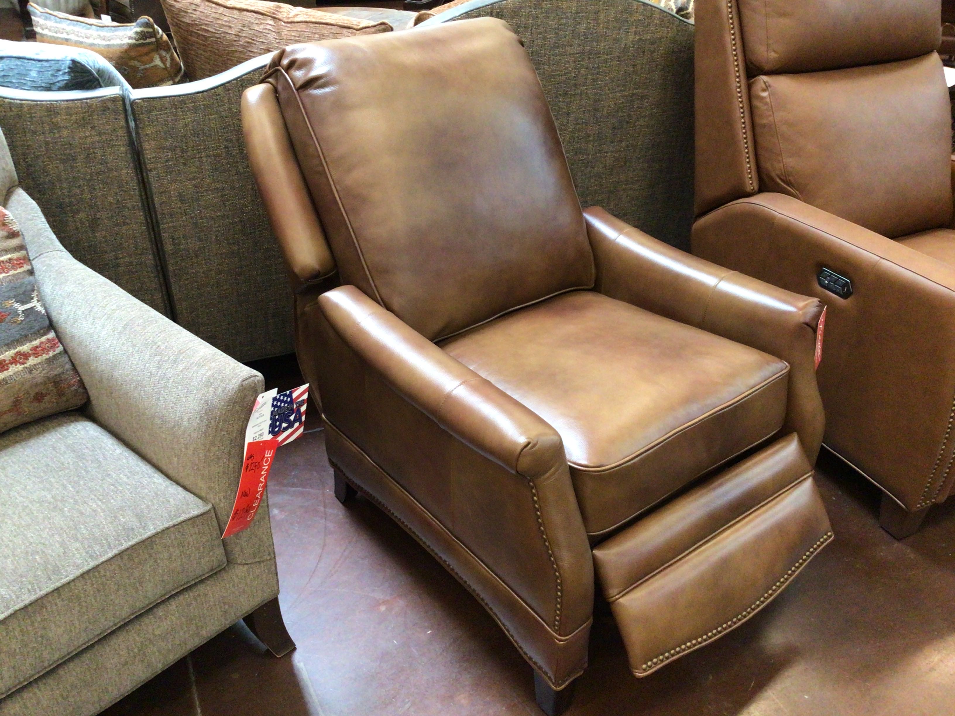 Brown leather recliner chair in a showroom setting with other furniture.