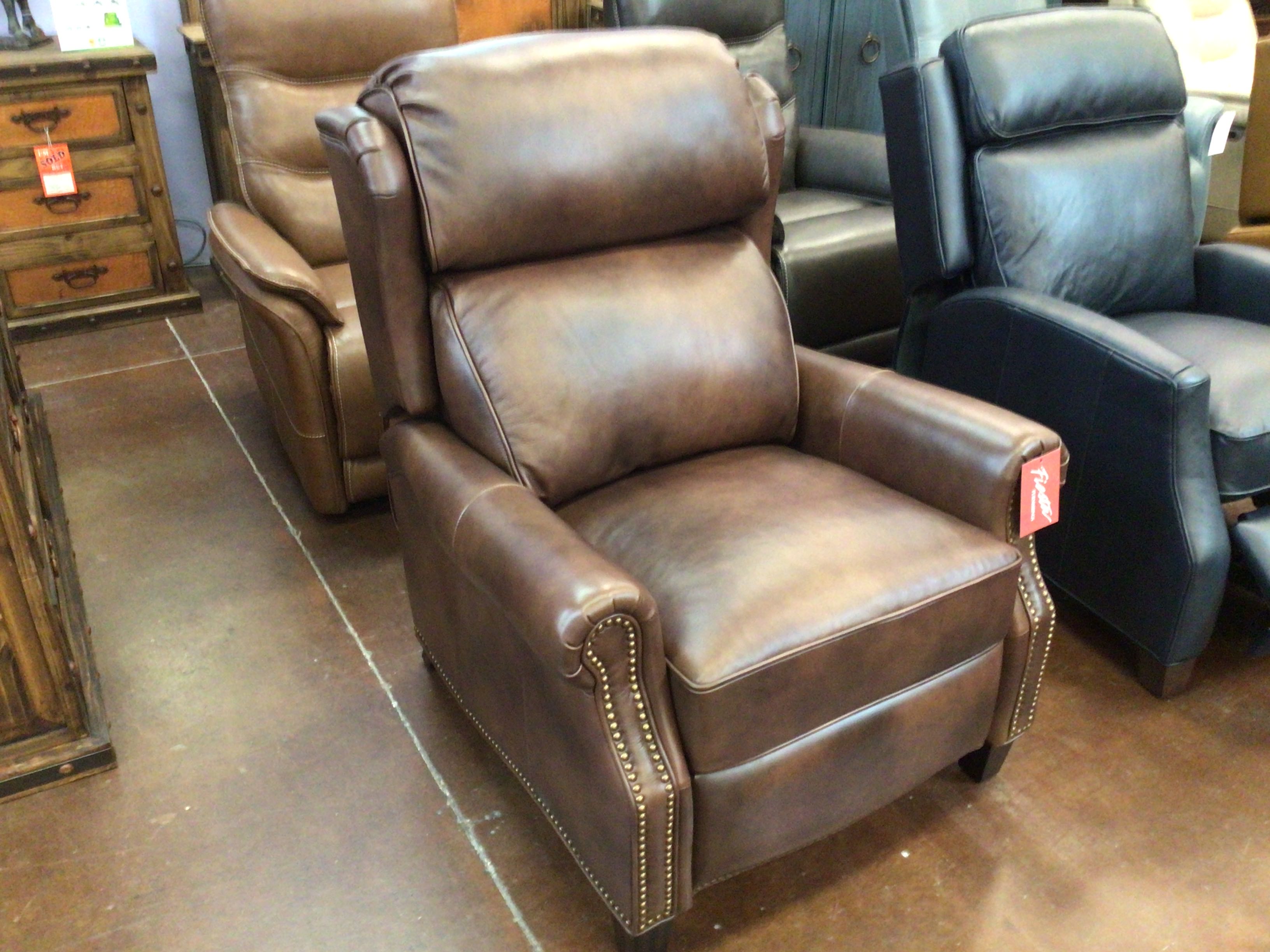 Brown leather recliner chair in a showroom setting with other furniture.