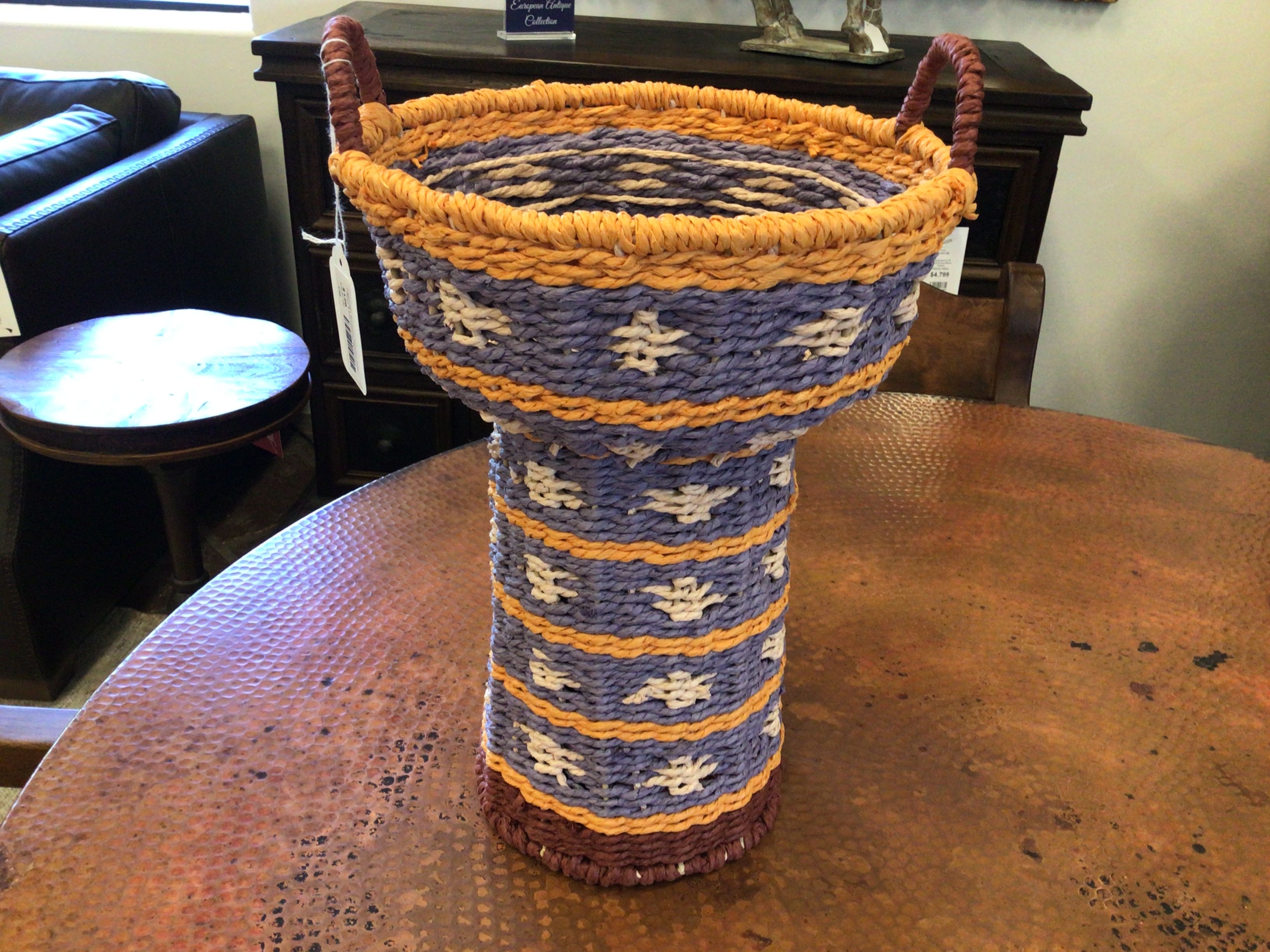 Decorative woven basket with blue and orange pattern on a wooden table.