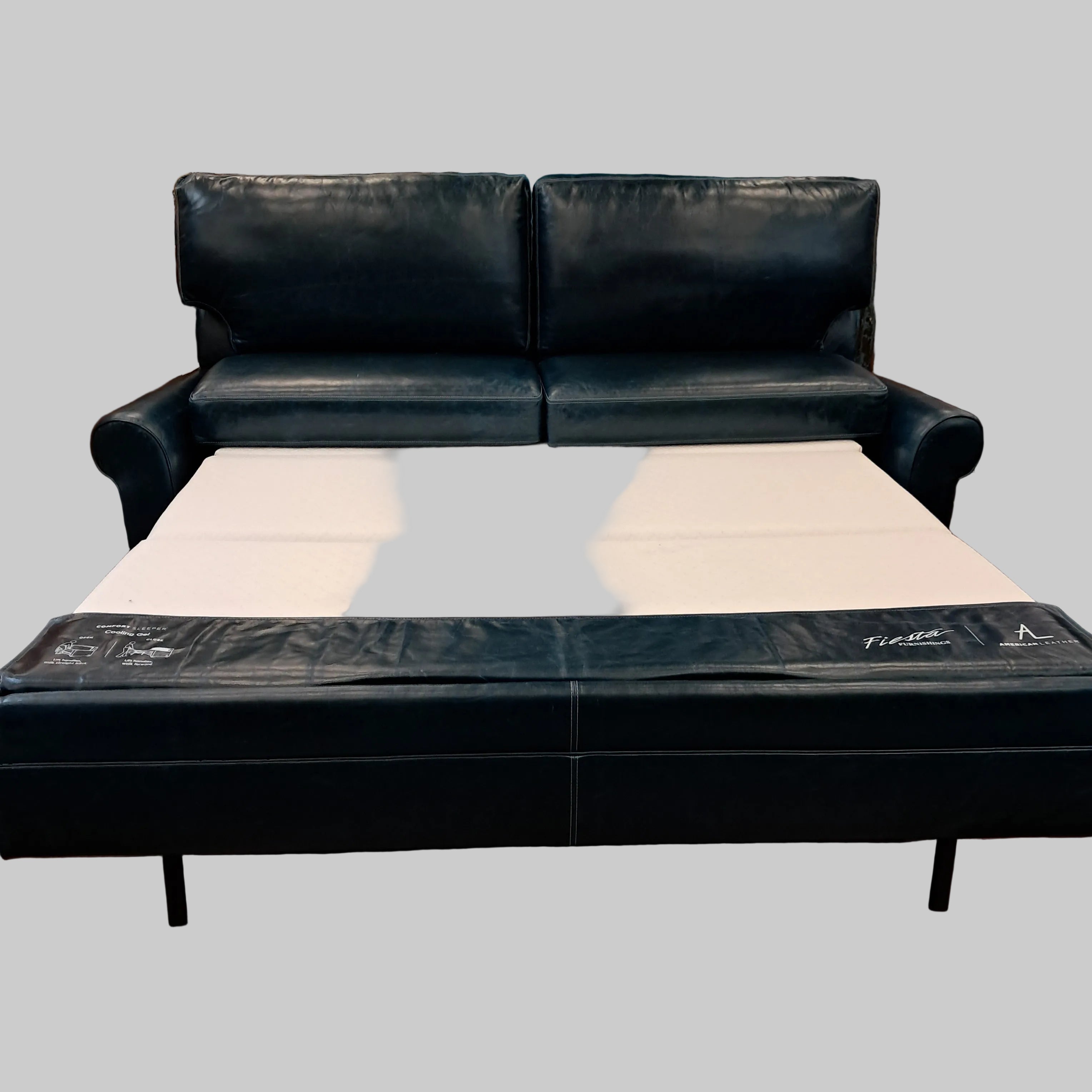 Black leather sectional sofa in a store setting with a white wall and shelves in the background.