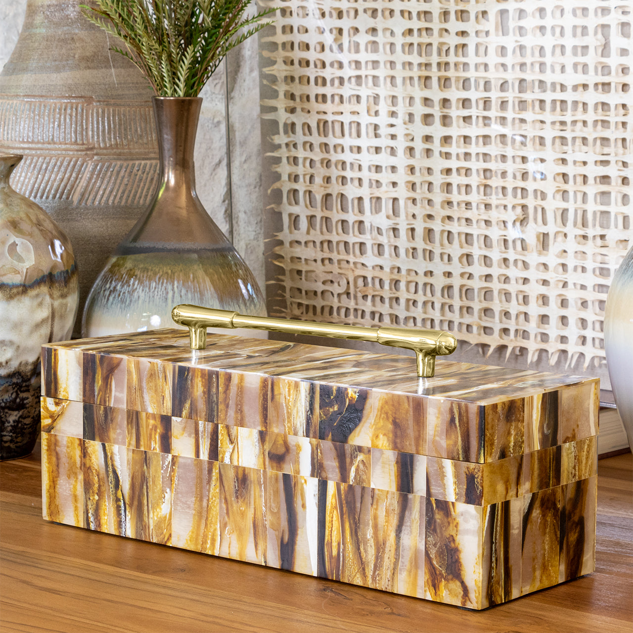 Decorative box with a gold handle on a wooden surface with decorative vases in the background.