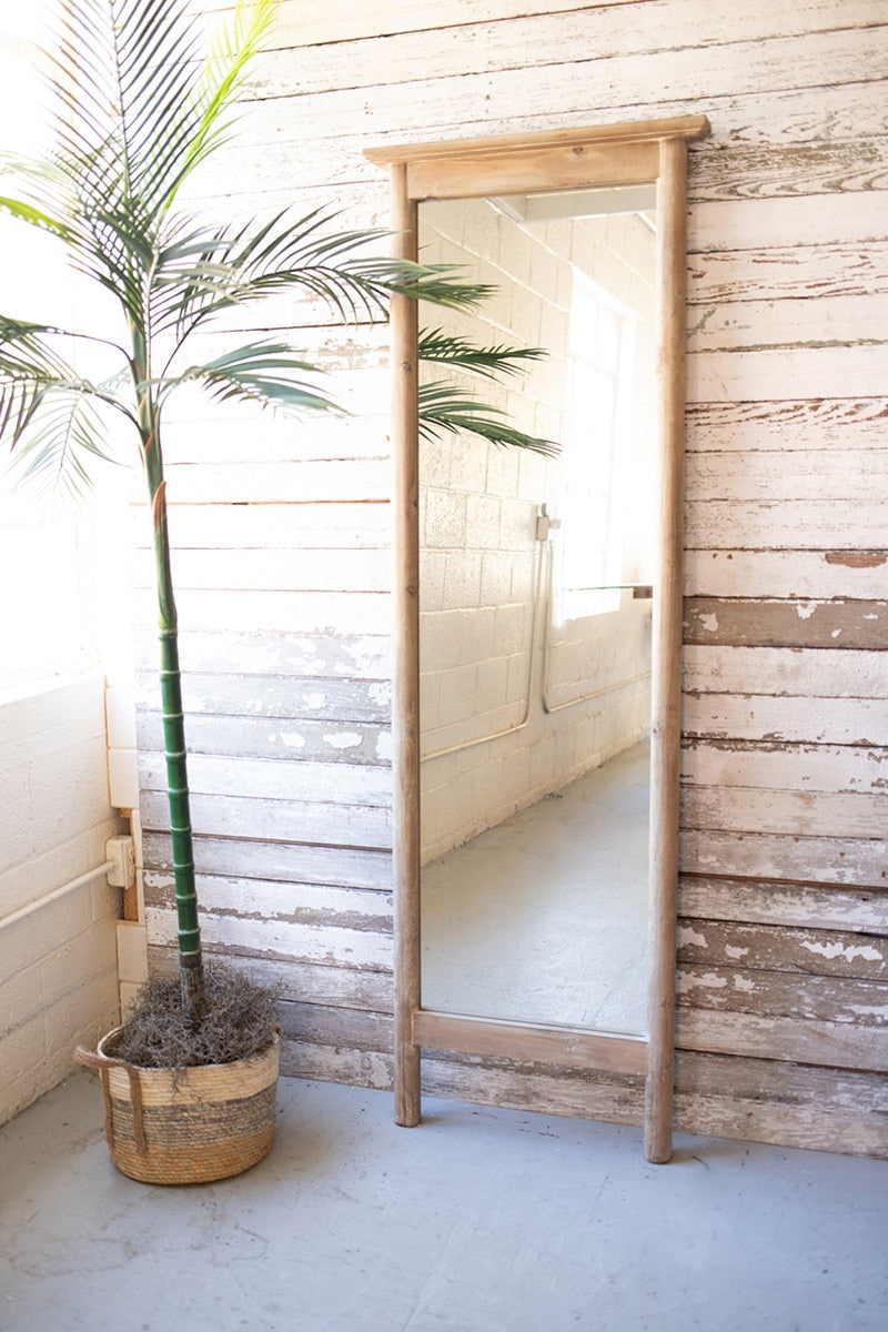 Wooden floor mirror leaning against a wooden wall with a potted plant nearby.