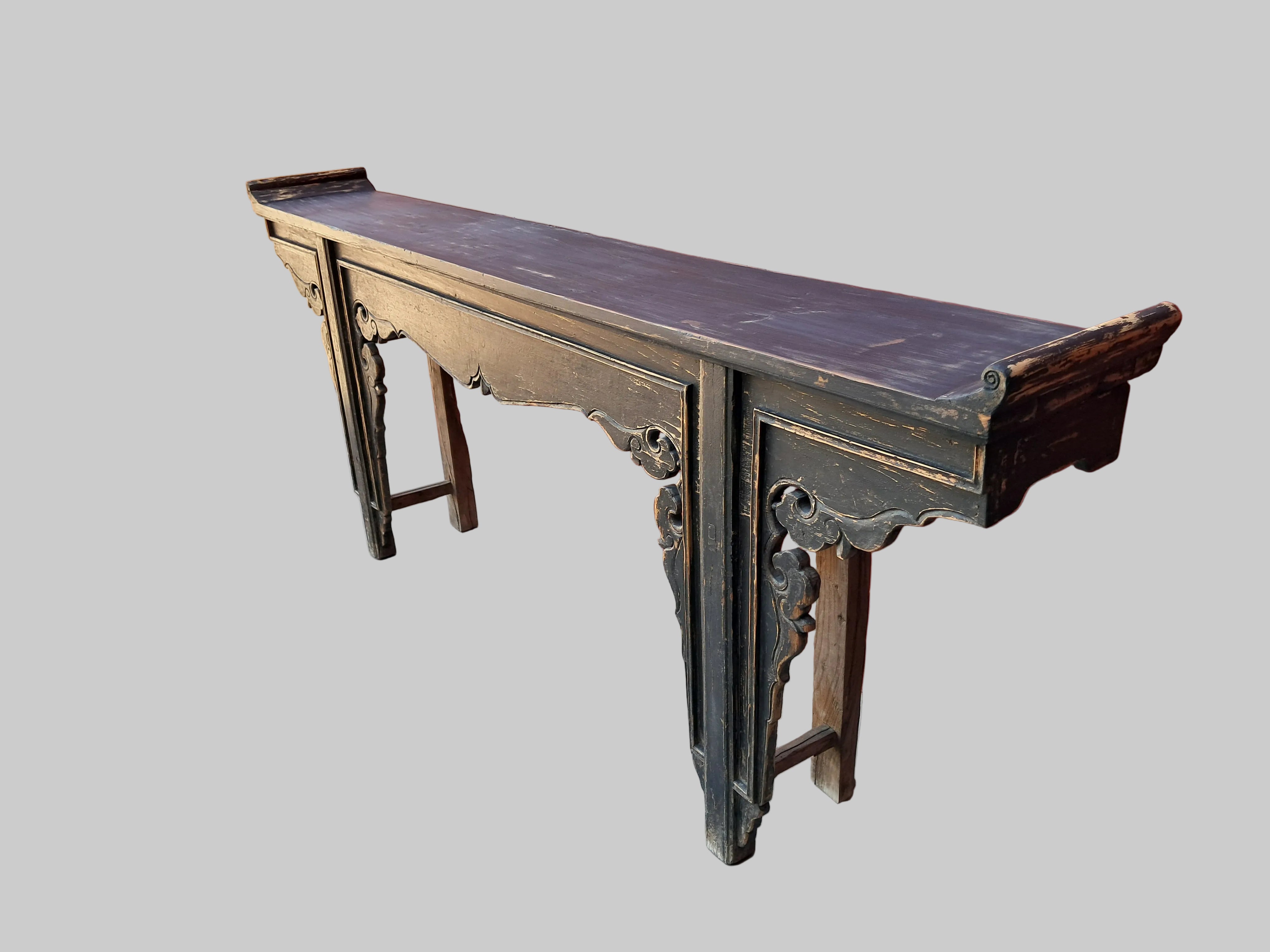Wooden console table with intricate carvings on a concrete floor against a red wall.