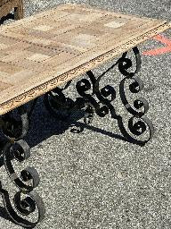 Coffee table with a pale parquet timber top on an ornate scrolled wrought iron base