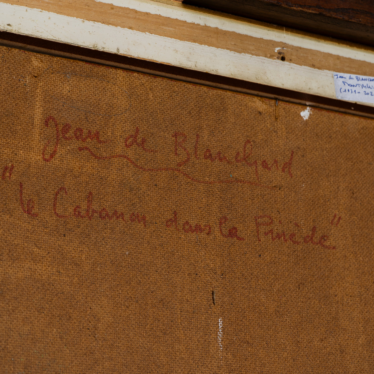 Close-up of a framed artwork or print showing a brown textured canvas with red handwritten script reading "Jean de Blanchard" and "Le Cabanon dans la Pinède".