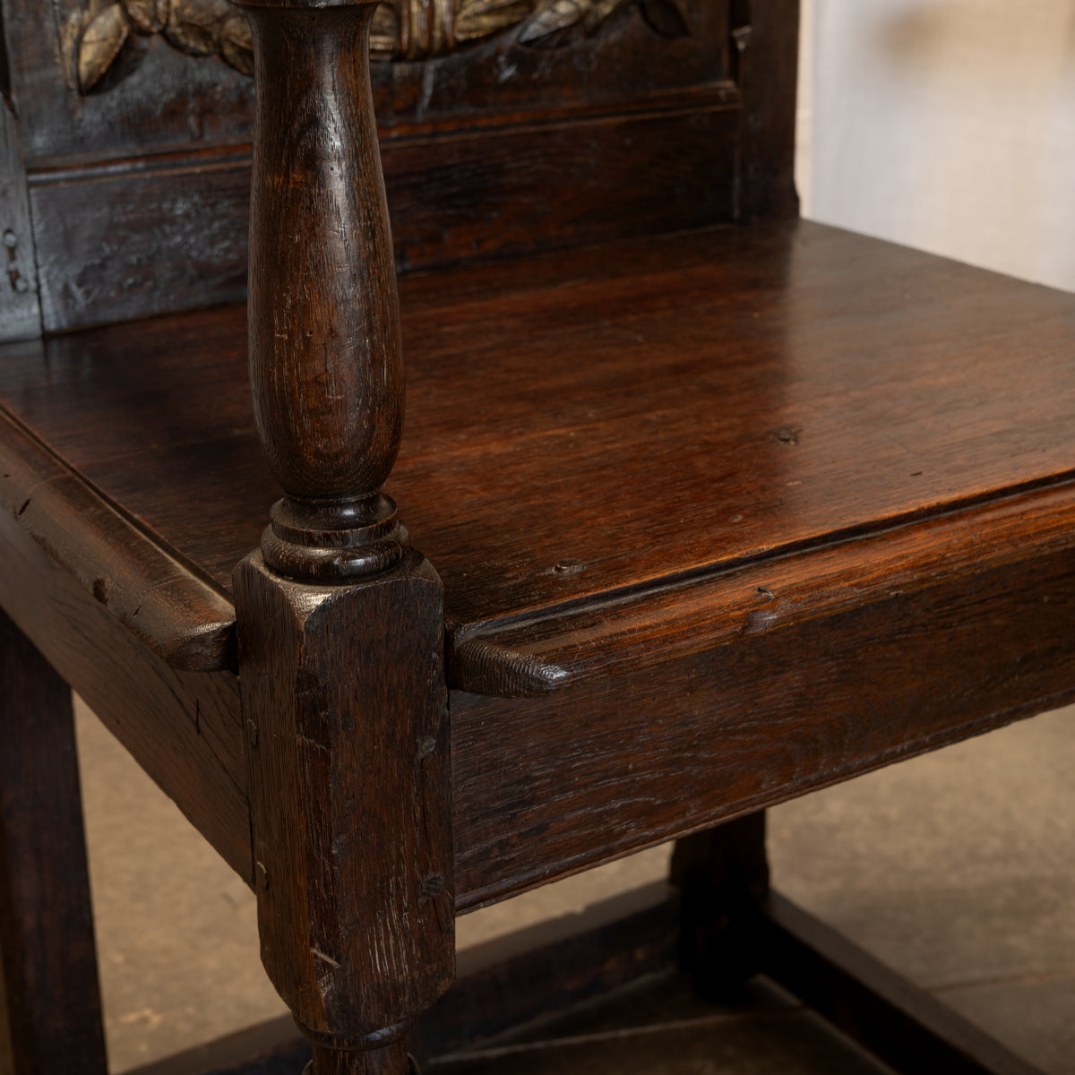 Close-up of a dark brown wooden chair showing the seat, carved backrest, turned leg post, and visible wood grain and wear.