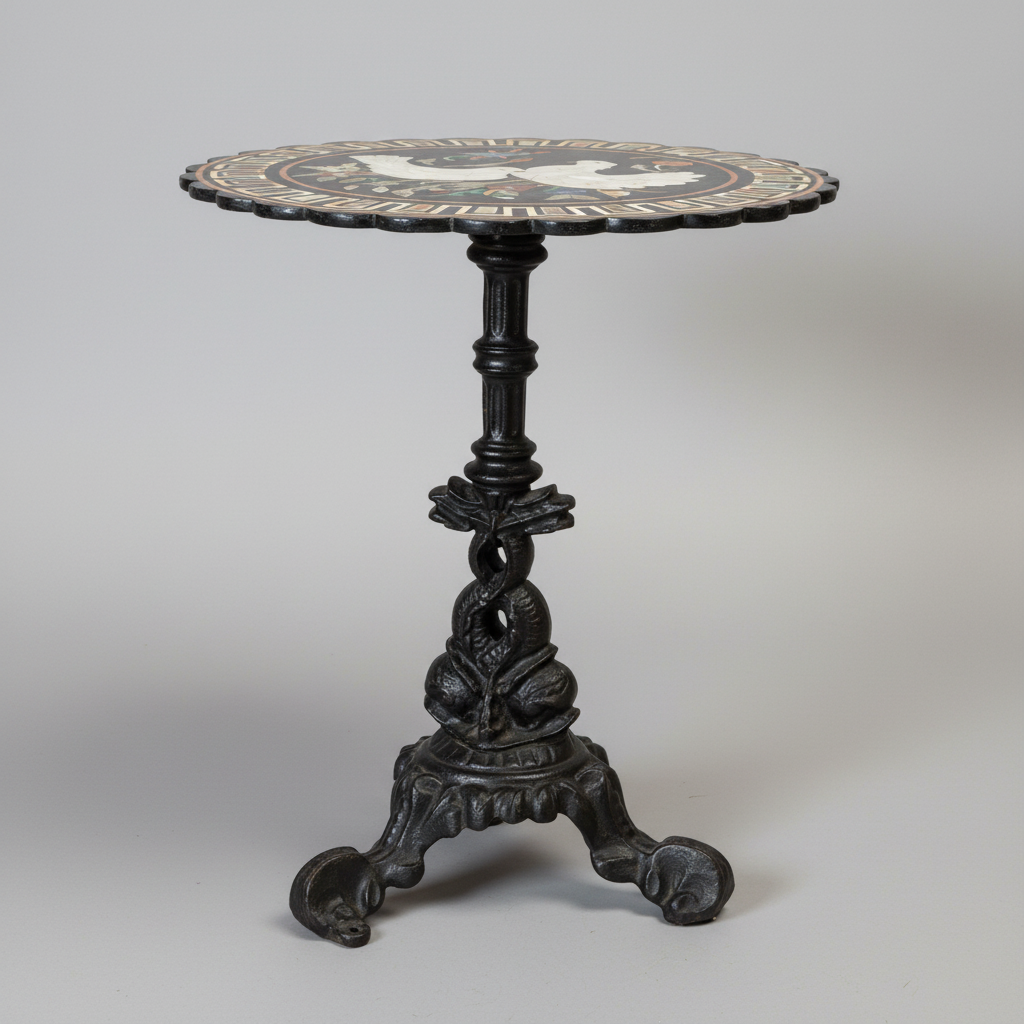 An antique pedestal table featuring a round inlaid top with a white stag and black border, supported by a dark cast-iron scrollwork base with three claw feet.