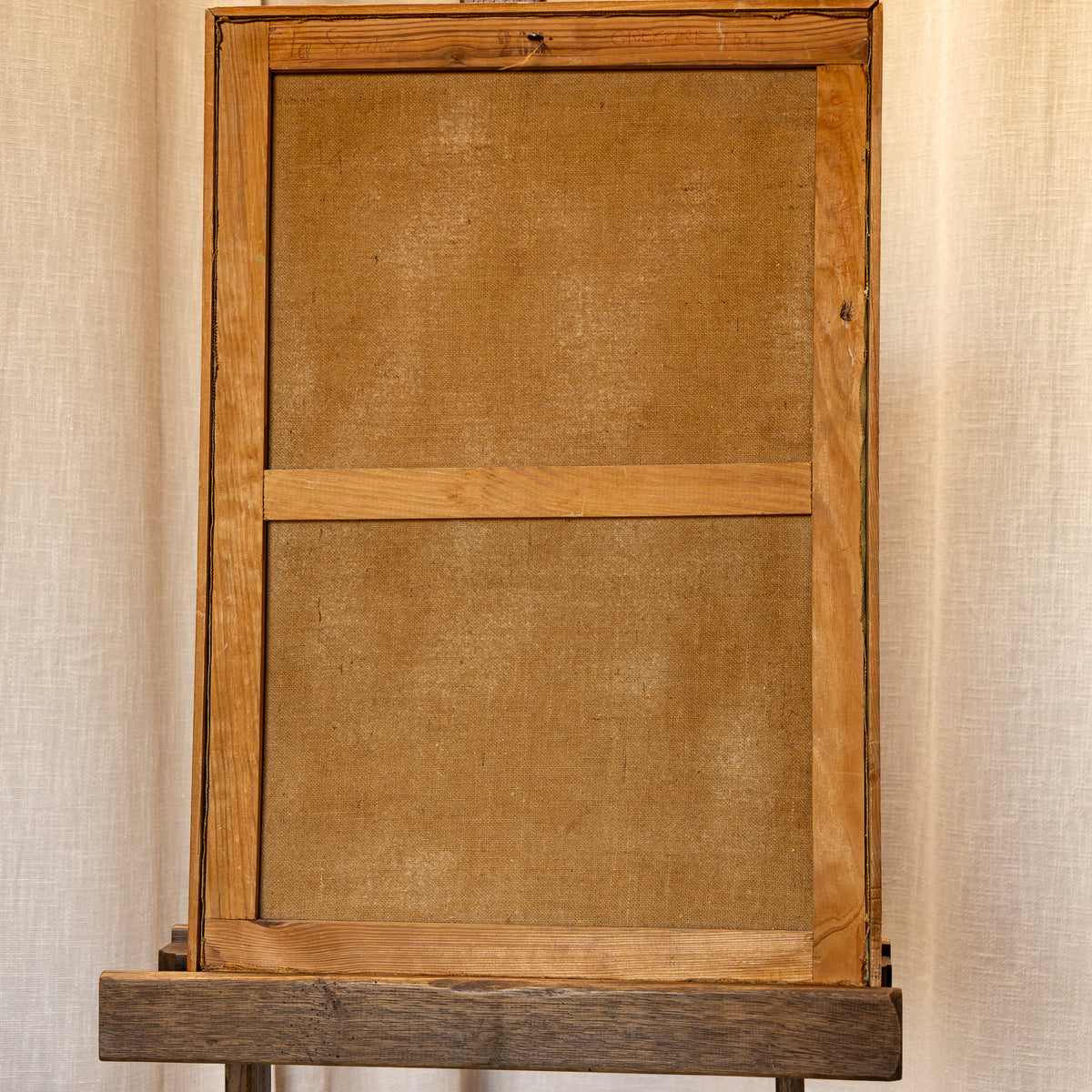 A rustic wooden picture frame with a linen canvas insert, displayed on a dark wooden stand against a neutral beige textured backdrop.