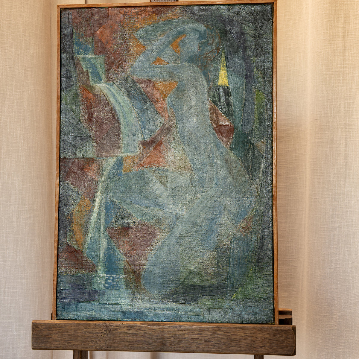An abstract painting of a seated female figure in muted blue, gray, rust, and green tones, displayed on a wooden easel against a beige textured curtain backdrop.