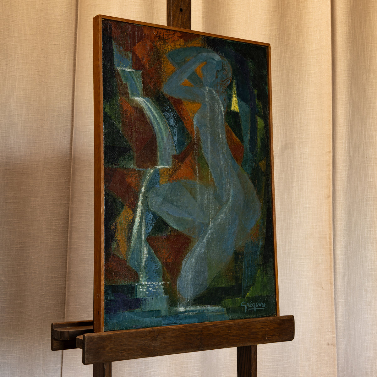 An abstract painting of a seated female figure in shades of blue, green, brown, and orange, displayed on a wooden easel against a beige fabric backdrop.