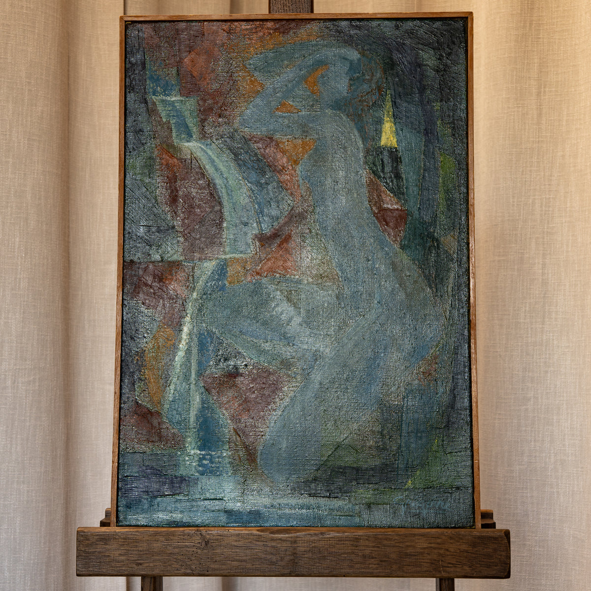 An abstract painting of a seated female figure in muted blue, gray, brown, and green tones, displayed on a wooden easel against a beige curtain backdrop.