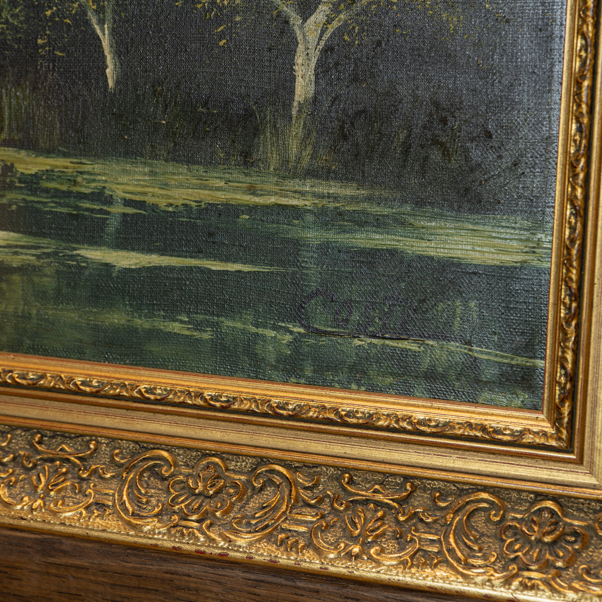 Close-up of an ornate gold-framed painting showing a dark green and black landscape with pale tree trunks and water reflections.