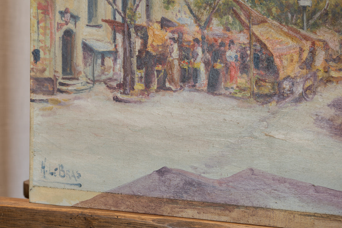 A close-up of a painted street scene with market stalls, figures, and buildings, showing visible canvas texture and a painted signature near the lower left.