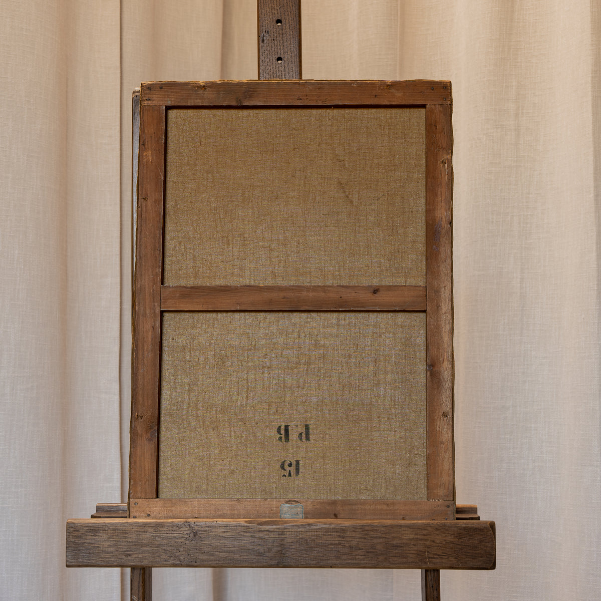 A rustic wooden display easel or stand with a linen-covered front panel, photographed against a neutral beige curtain backdrop.