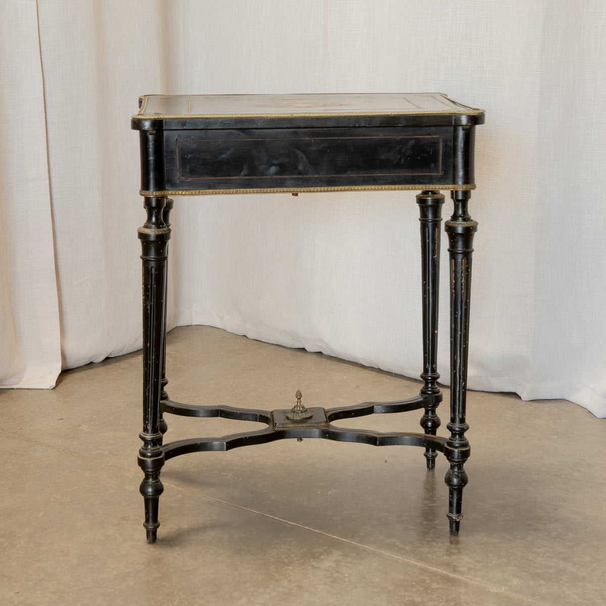 An antique black wooden writing desk with turned legs and brass trim, set against a draped white fabric backdrop.