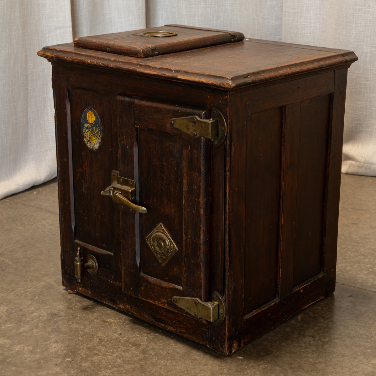 An antique dark brown wooden safe or cash box with brass hardware, photographed against a neutral draped fabric backdrop.