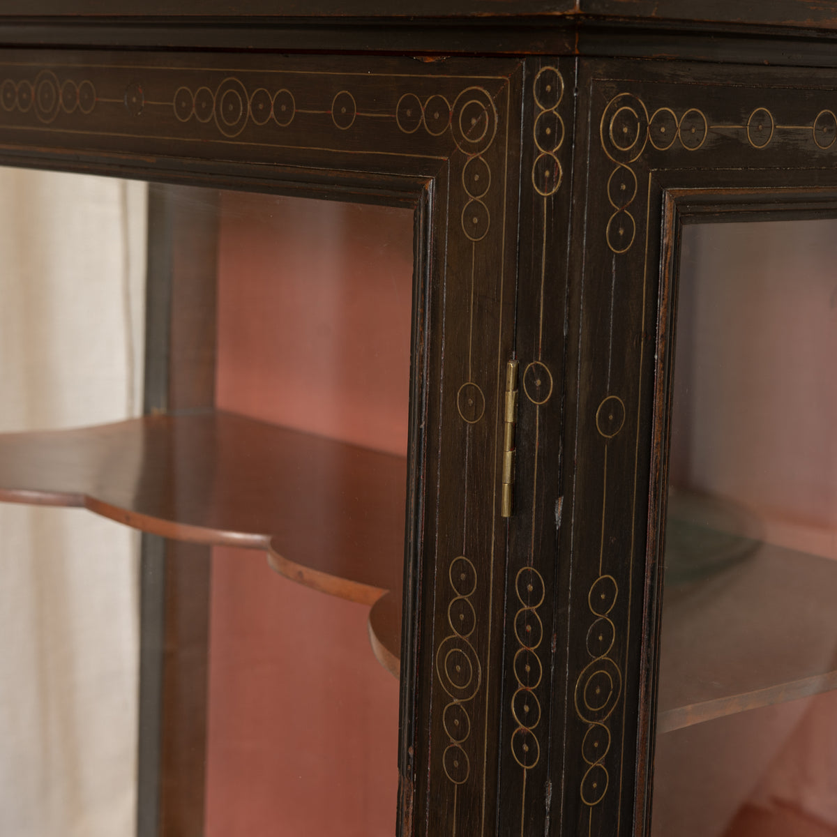 Close-up of a dark wood display cabinet with glass doors and brass hardware, showing decorative gold-toned circular inlays and a wooden shelf inside.