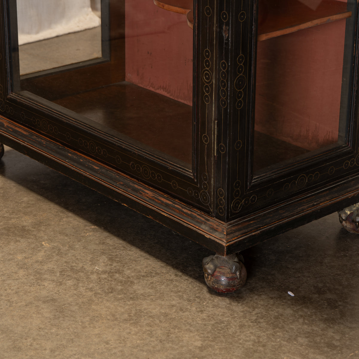 Close-up of a dark wooden display cabinet with glass doors and carved feet, showing the lower corner and interior shelving.