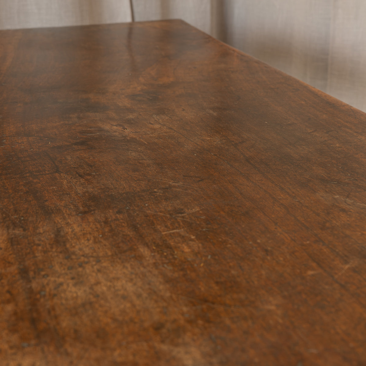 A close-up view of a dark brown wooden tabletop with visible grain and wear marks, set against a softly blurred neutral indoor background.
