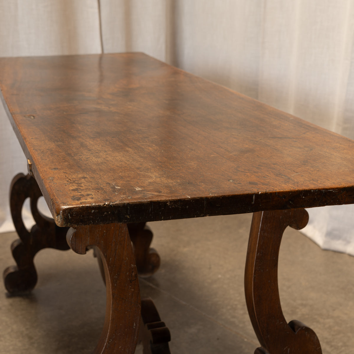 An antique dark brown wooden table with ornate carved legs and a weathered, rustic finish, photographed against a neutral draped fabric backdrop.