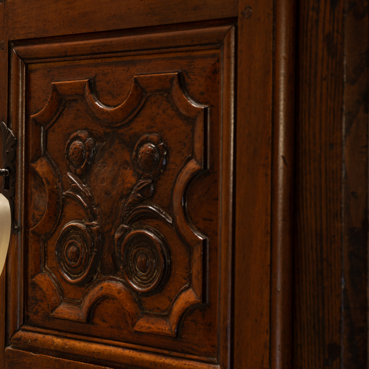 Close-up of a dark brown carved wooden cabinet door with ornate floral and scroll motifs, showing rich wood grain and polished finish.