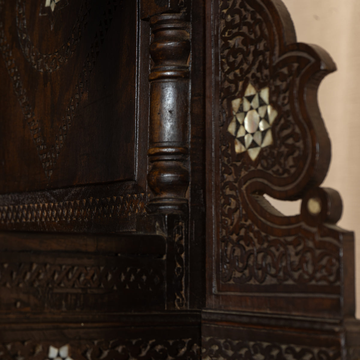 Close-up of an ornate dark carved wooden cabinet corner with intricate floral inlay details and turned wooden posts.
