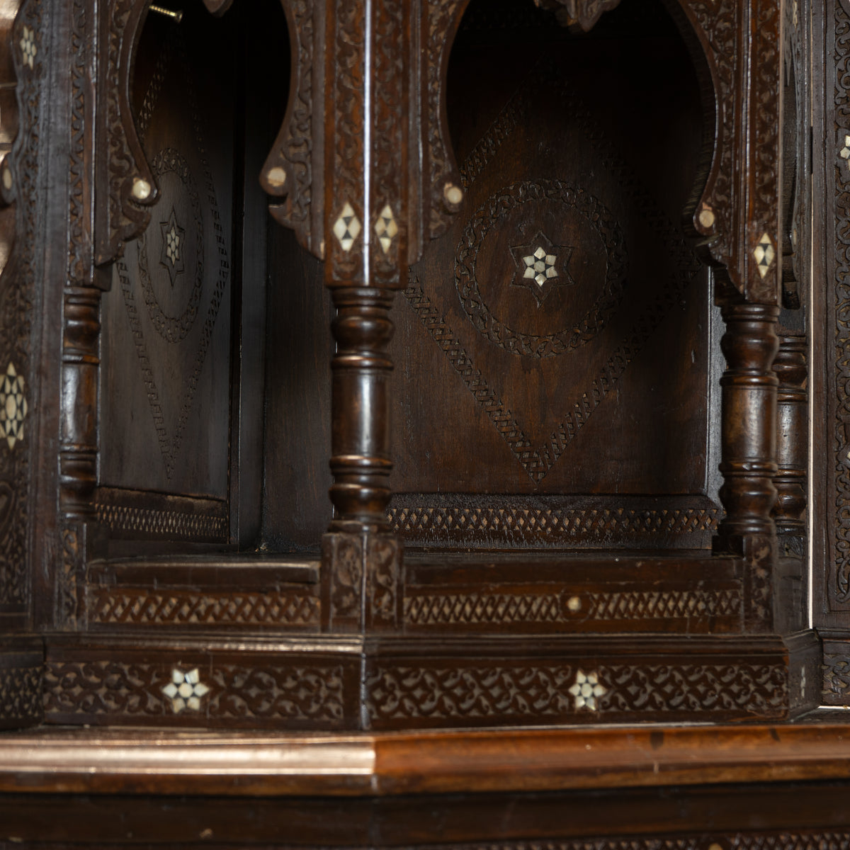 Close-up of an ornate dark carved wooden cabinet or hutch with arched niches, intricate floral inlay details, and turned legs.