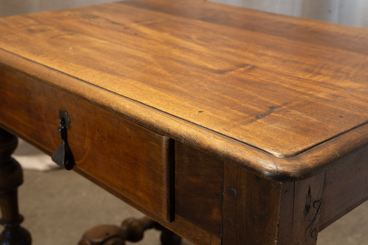Close-up of a rustic wooden writing desk with a single drawer, featuring a warm medium-brown finish, dark metal drawer pull, and a raised bevelled edge.