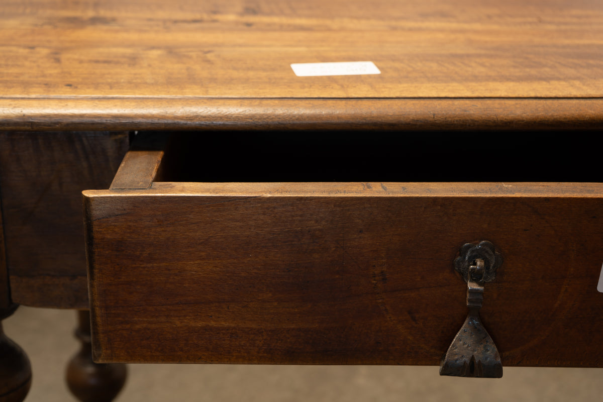 Close-up of a dark brown wooden desk or cabinet with an open drawer and a dark metal pull handle, showing the wood grain and a small white price tag on the tabletop.