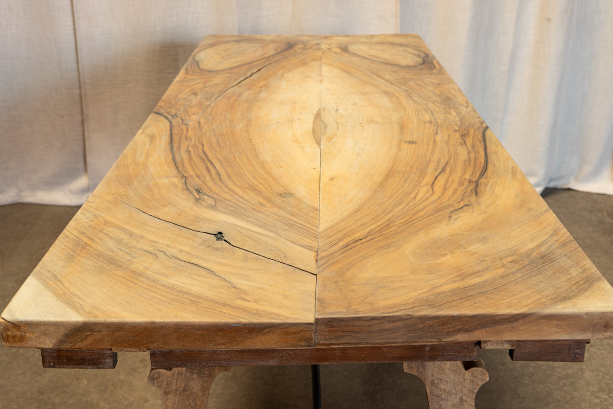 A rustic wooden table made from two large, thick live-edge wood slabs joined in the center, showing prominent natural grain patterns and knots. The table is photographed from a top-down perspective against a neutral draped fabric backdrop.