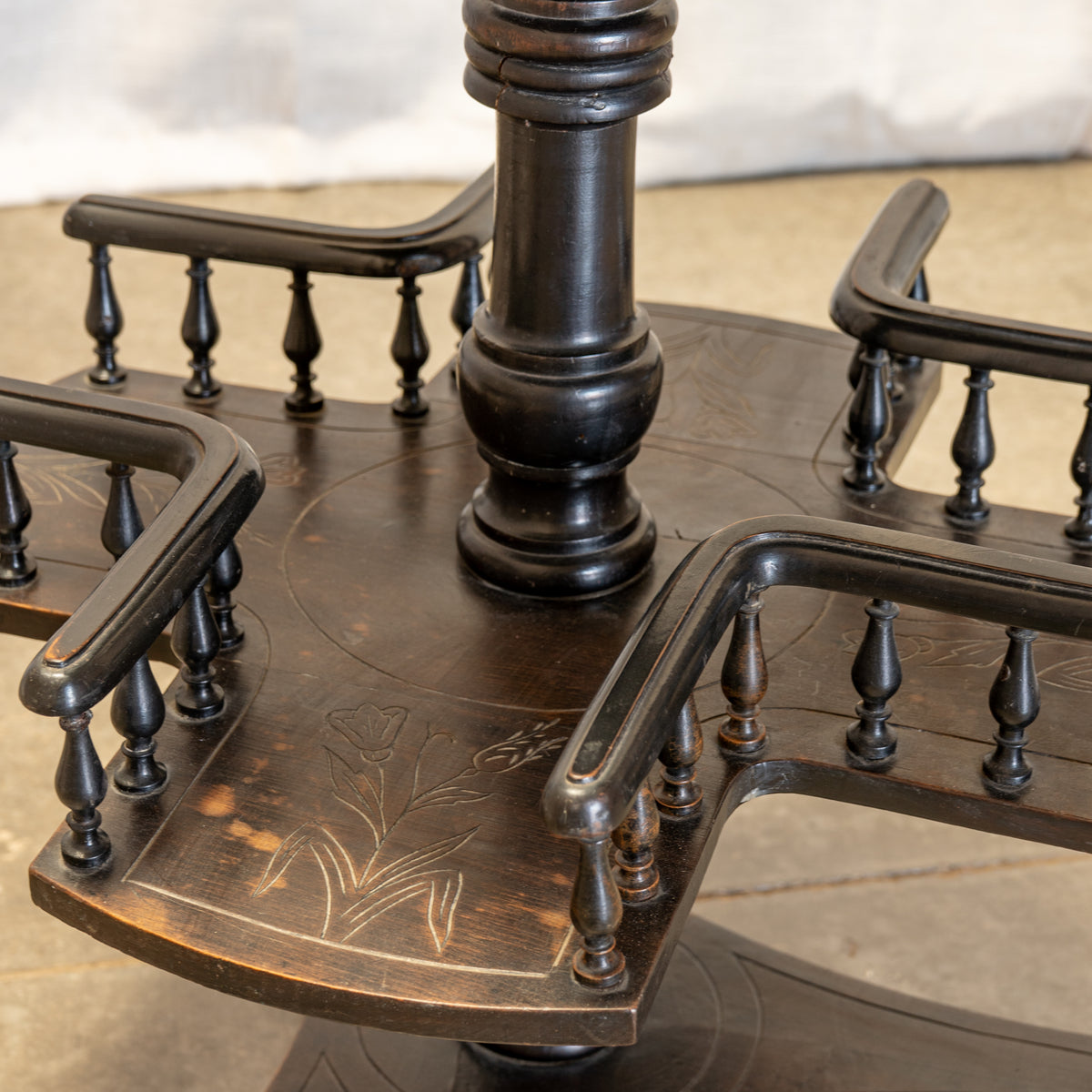 Close-up of a dark carved wooden table base with four curved armrests and a central pedestal, showing engraved floral details and a polished finish.