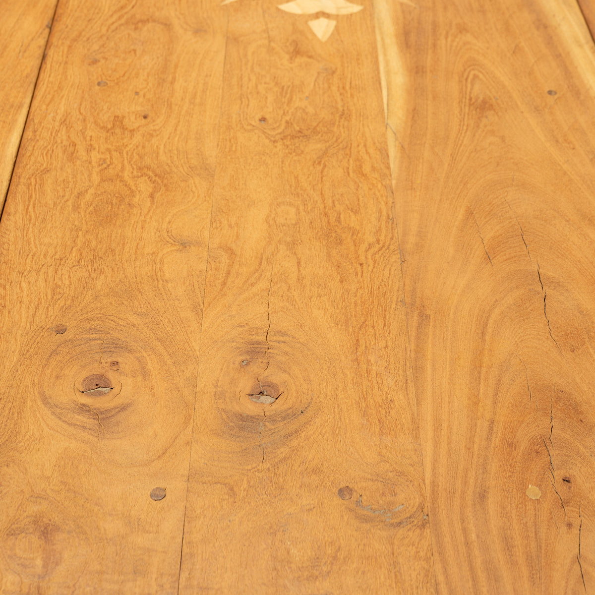 Close-up of a warm honey-toned wood surface with visible grain, knots, and plank seams, likely a tabletop or flooring sample.
